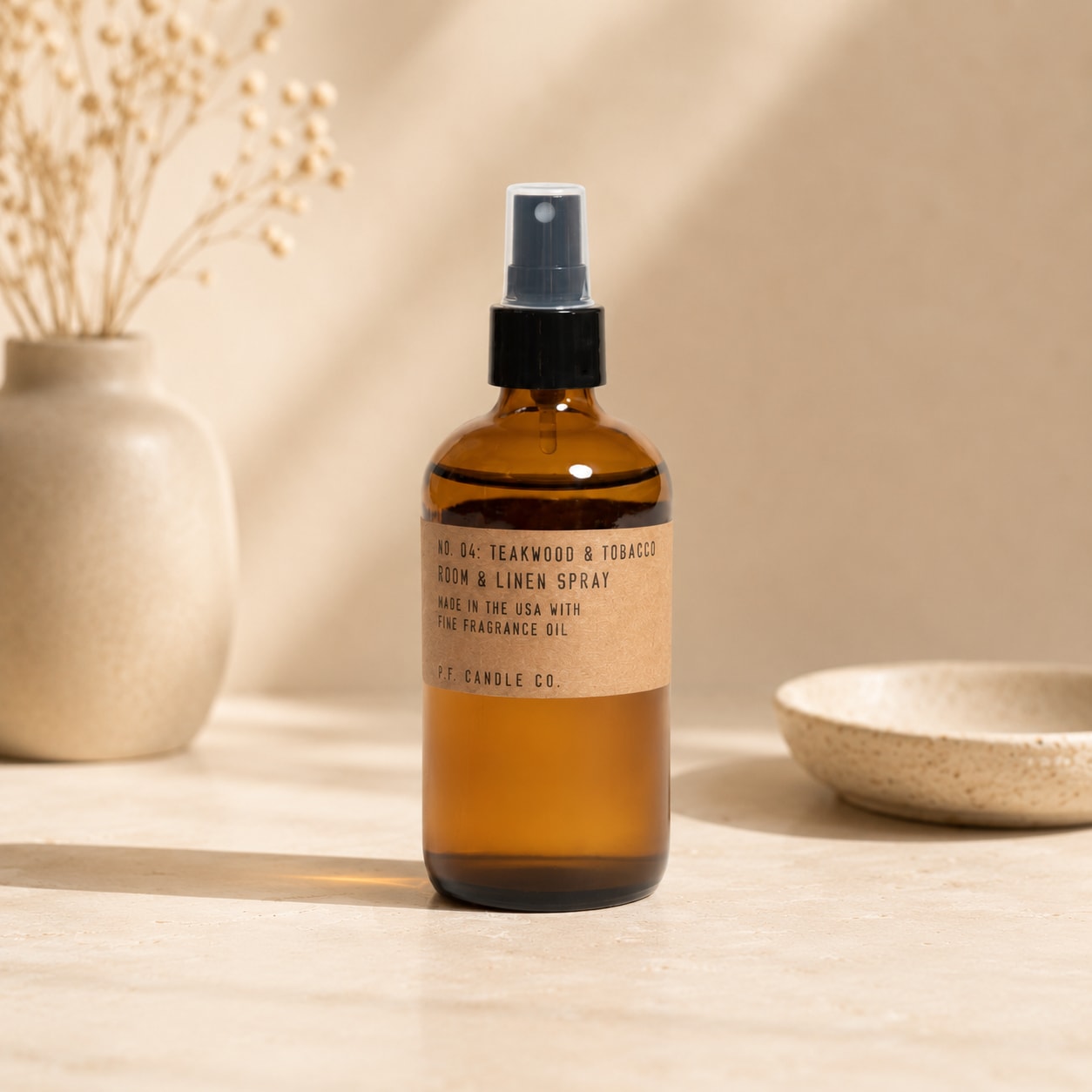 Amber room spray bottle on a neutral tabletop with a vase and bowl nearby