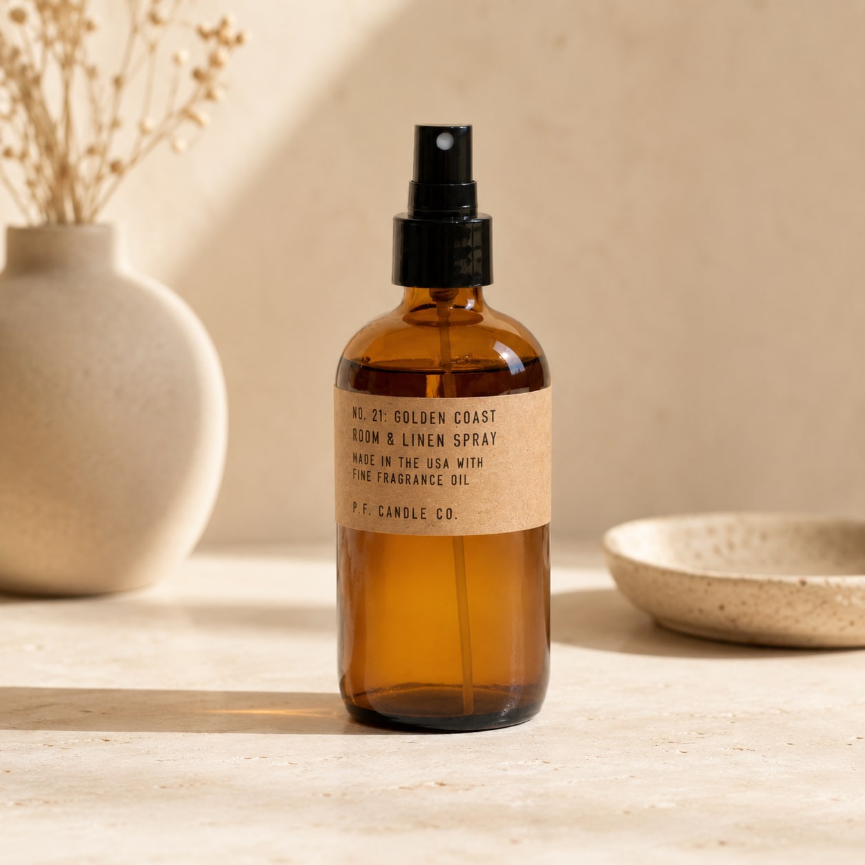 Amber room spray bottle with black pump on a neutral tabletop