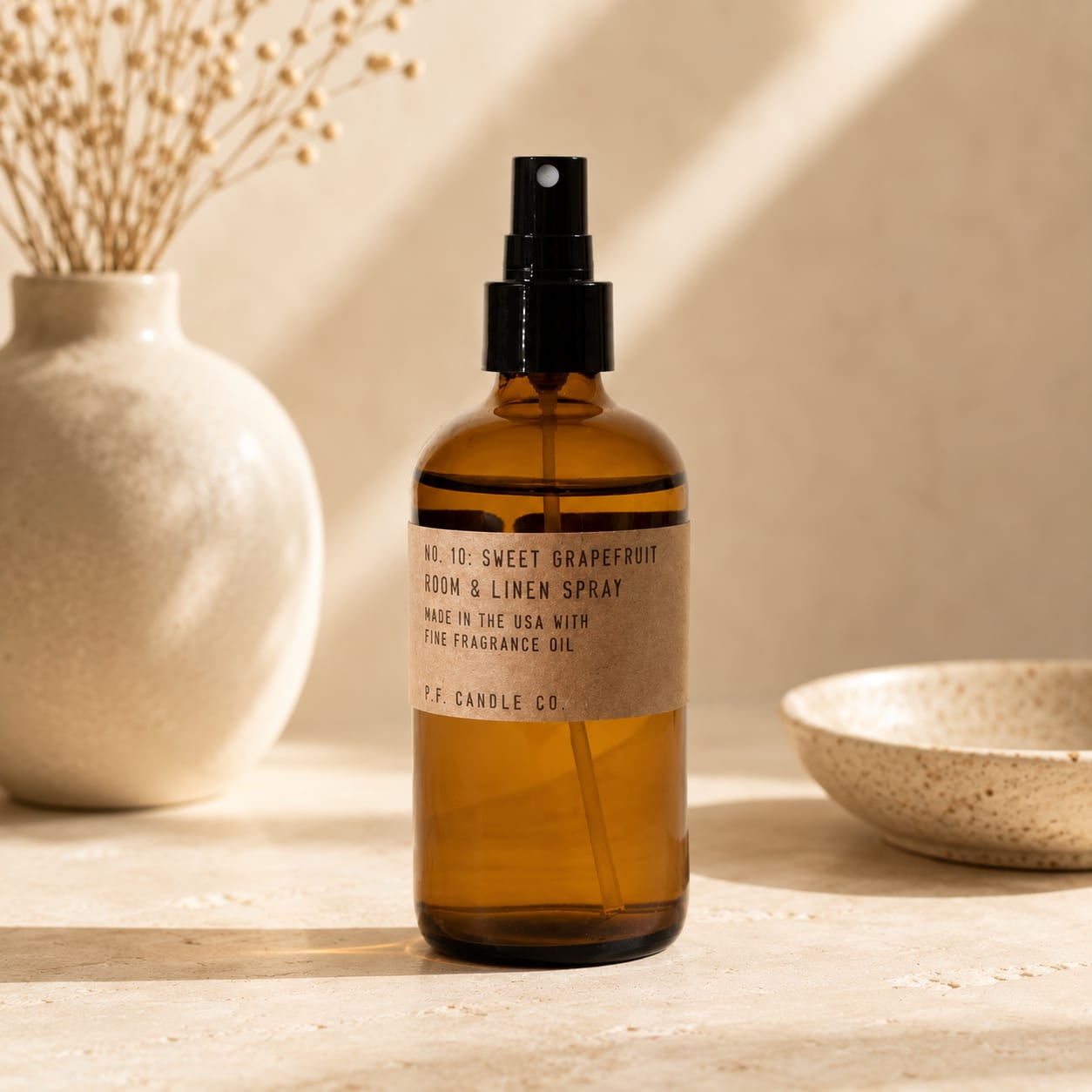 Amber room spray bottle with black pump on a neutral tabletop