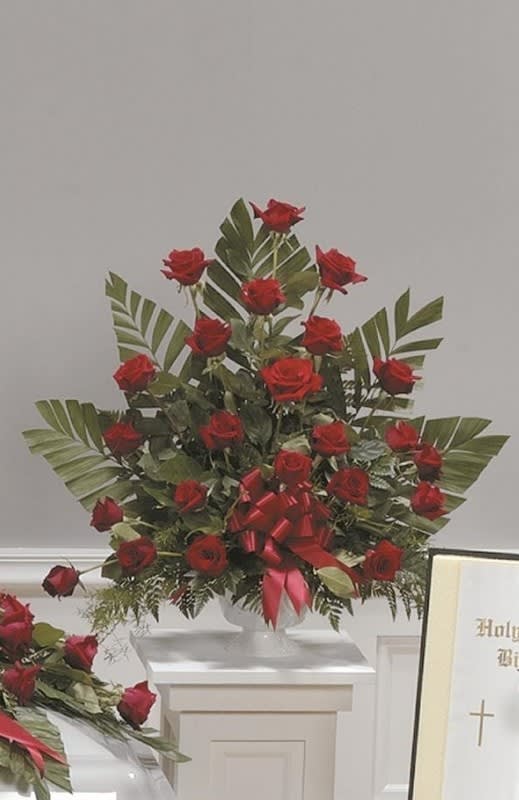 Tall arrangement of red roses with a red ribbon on a white pedestal