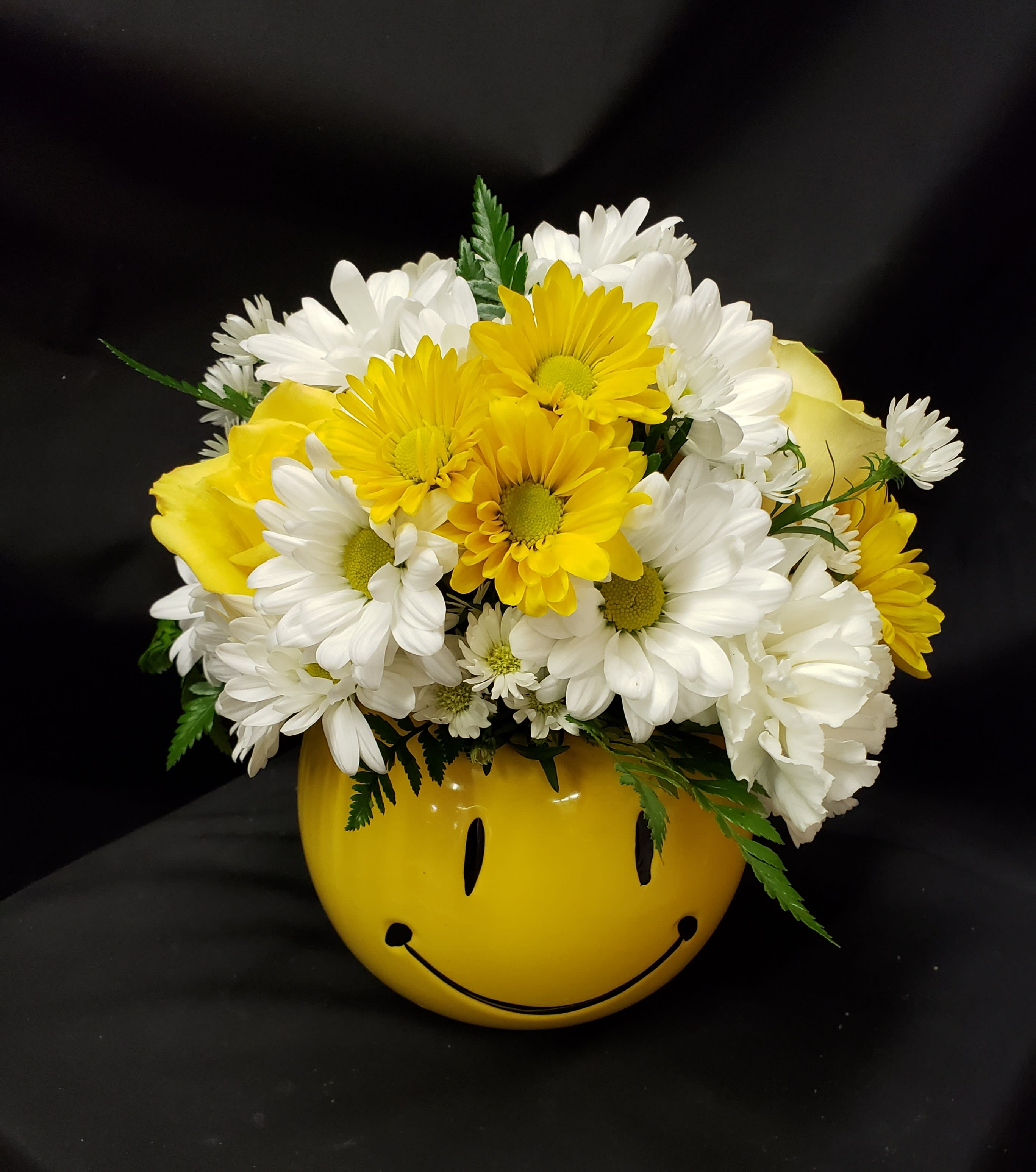 Yellow and white daisy bouquet in a smiley-face vase