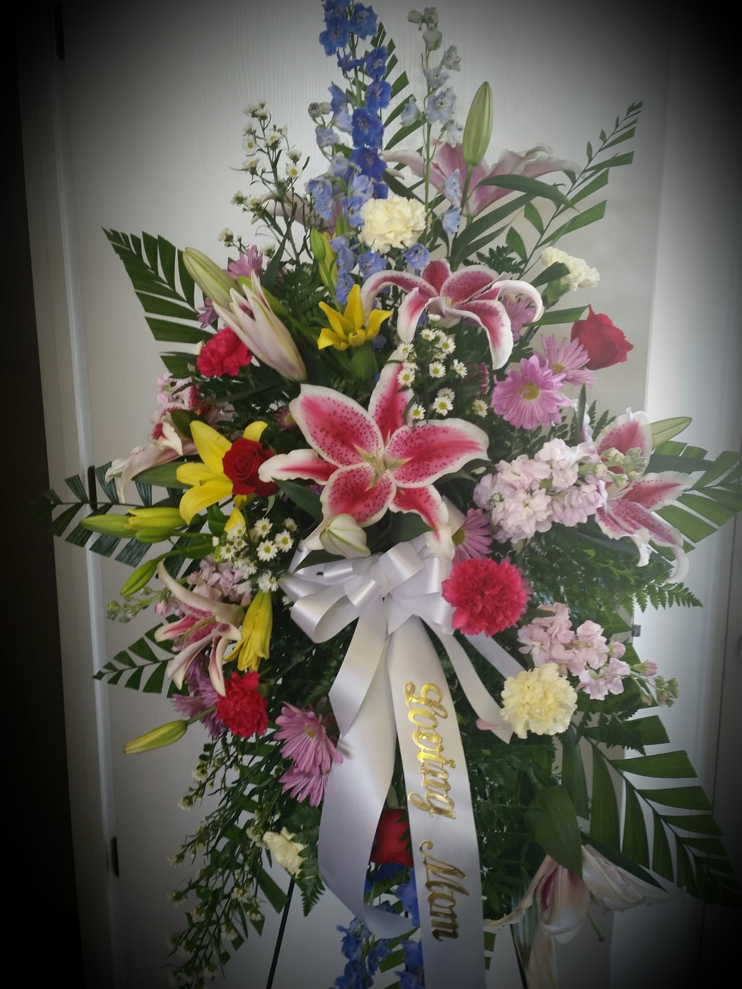 Tall mixed flower standing spray with lilies, roses, and a white ribbon
