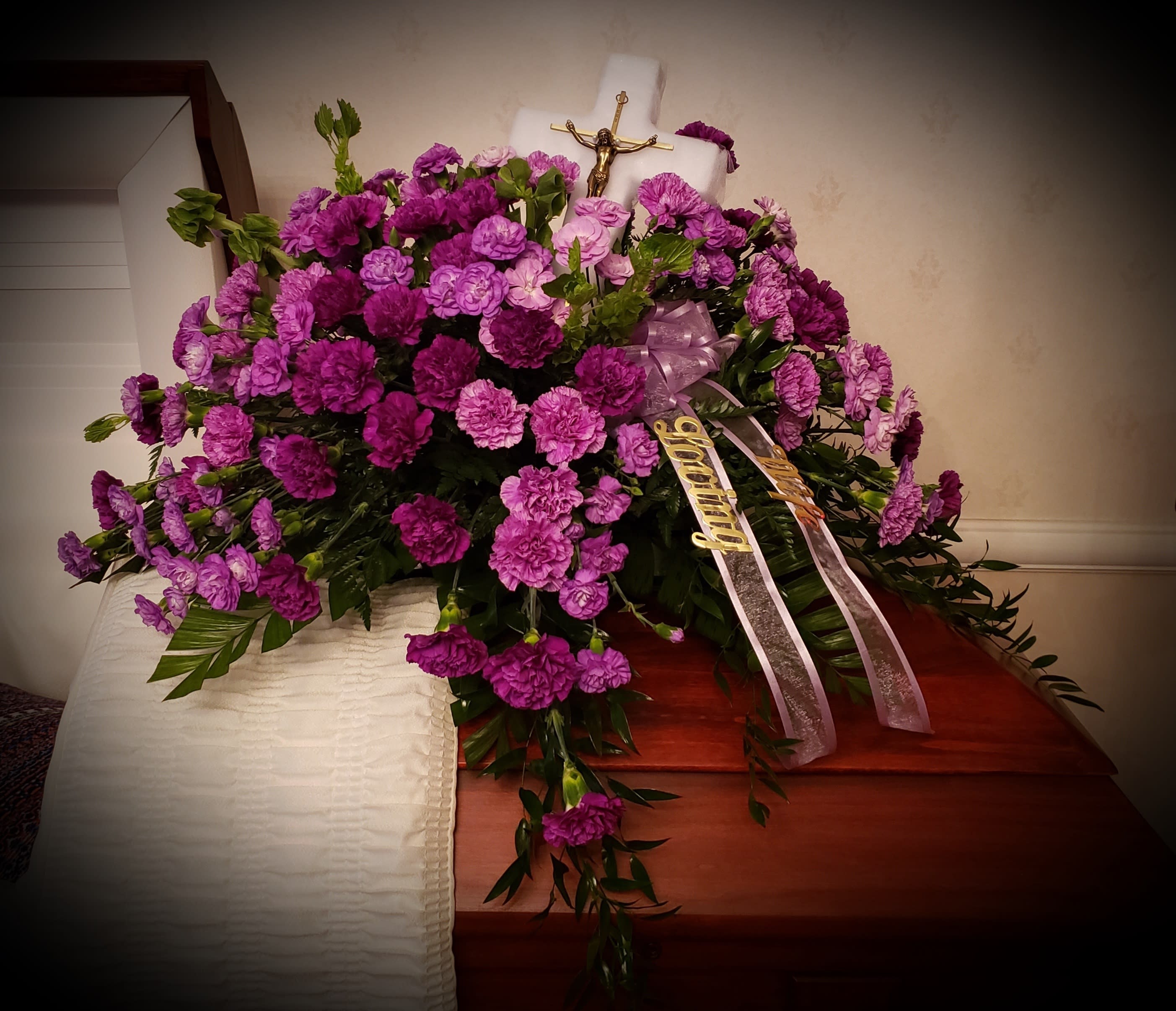 Purple carnation funeral spray with ribbons on a casket