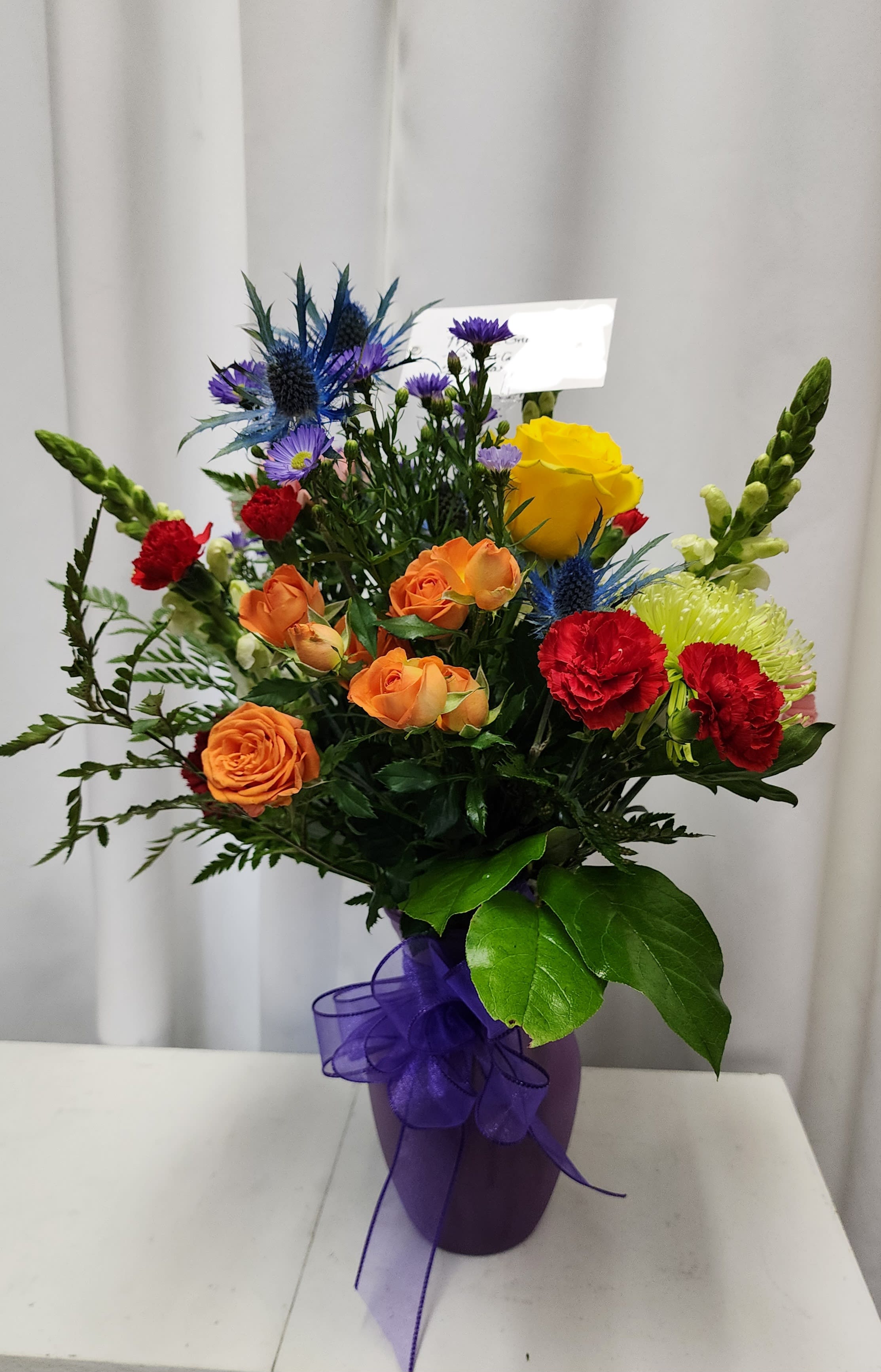 Mixed bouquet of roses, carnations, and blue thistle in a purple vase