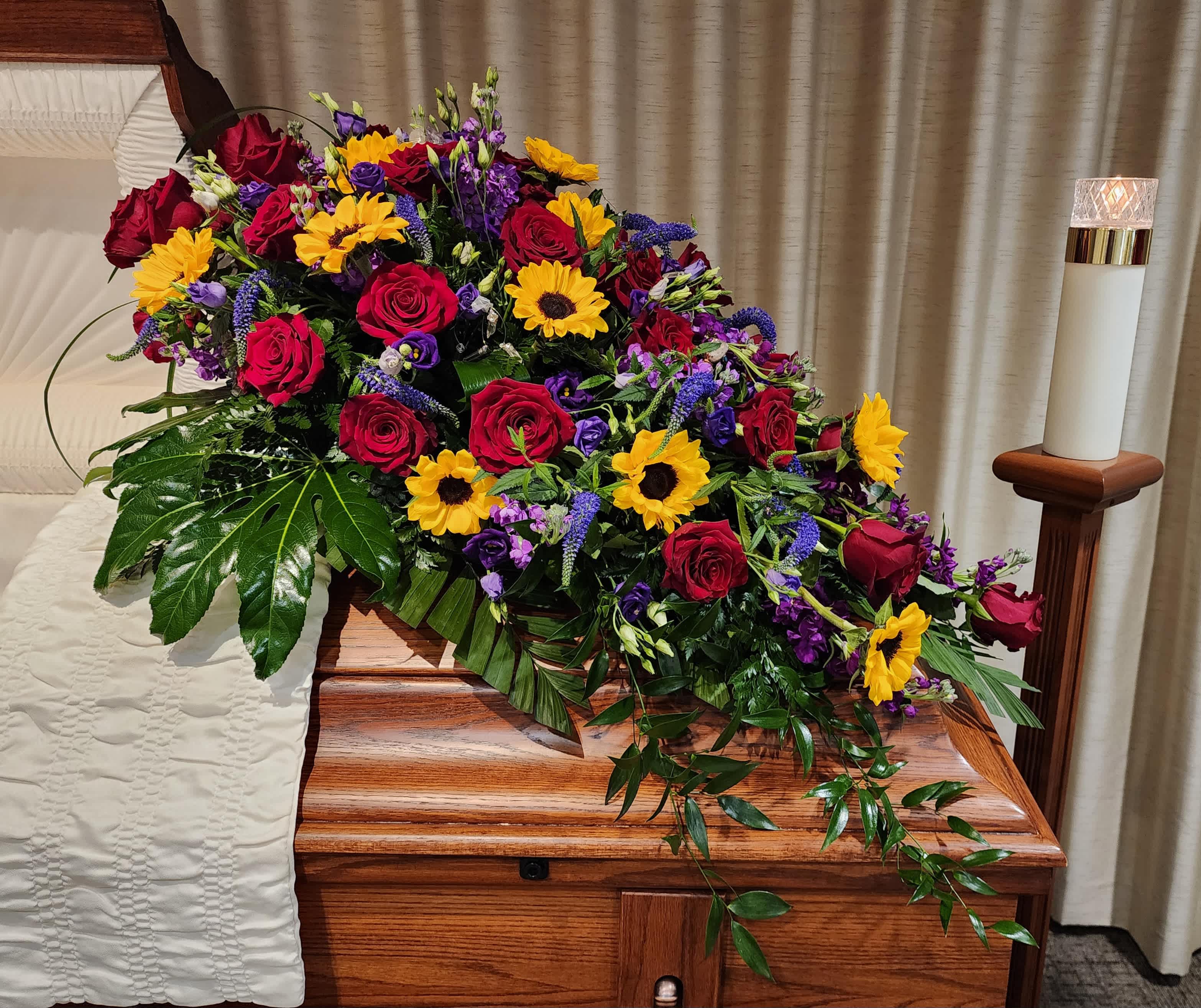 Casket spray with red roses, sunflowers, and purple flowers