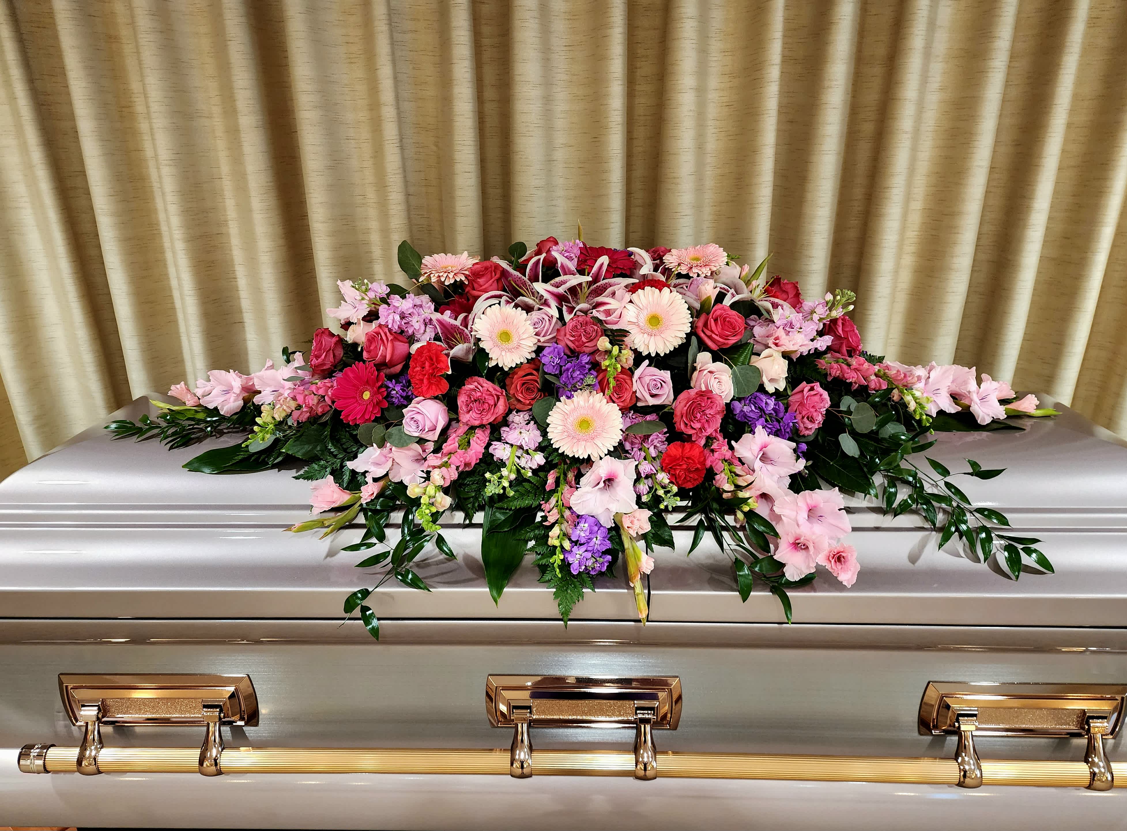 Pink and red floral casket spray on a silver casket