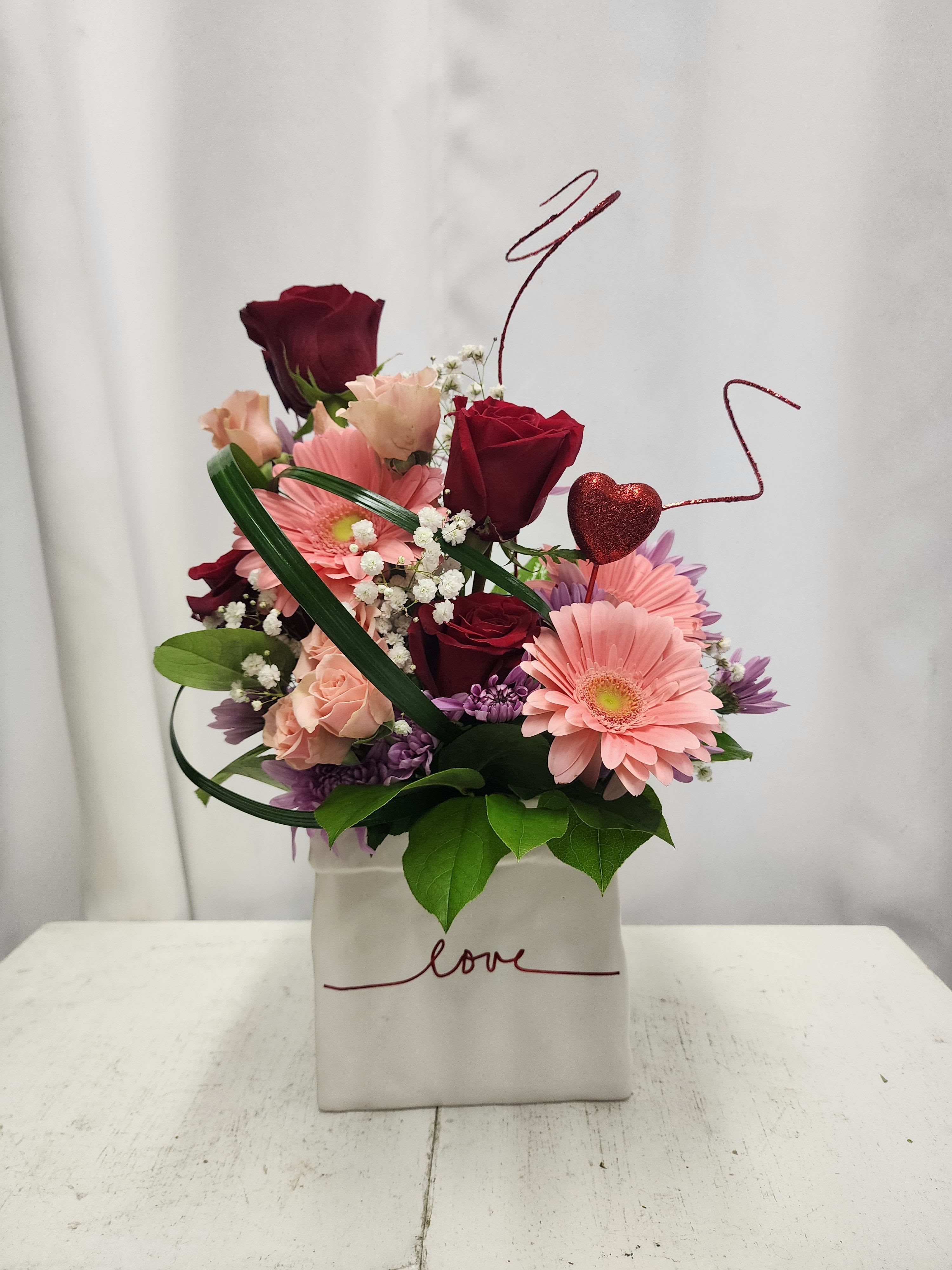 Pink and burgundy flower arrangement in a white box with a heart pick