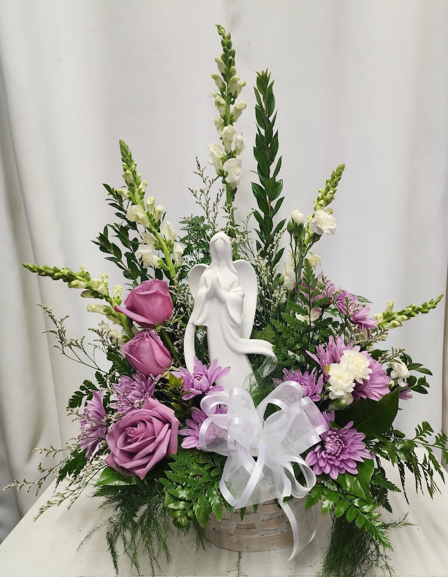 Purple and white floral arrangement with an angel figurine in a basket