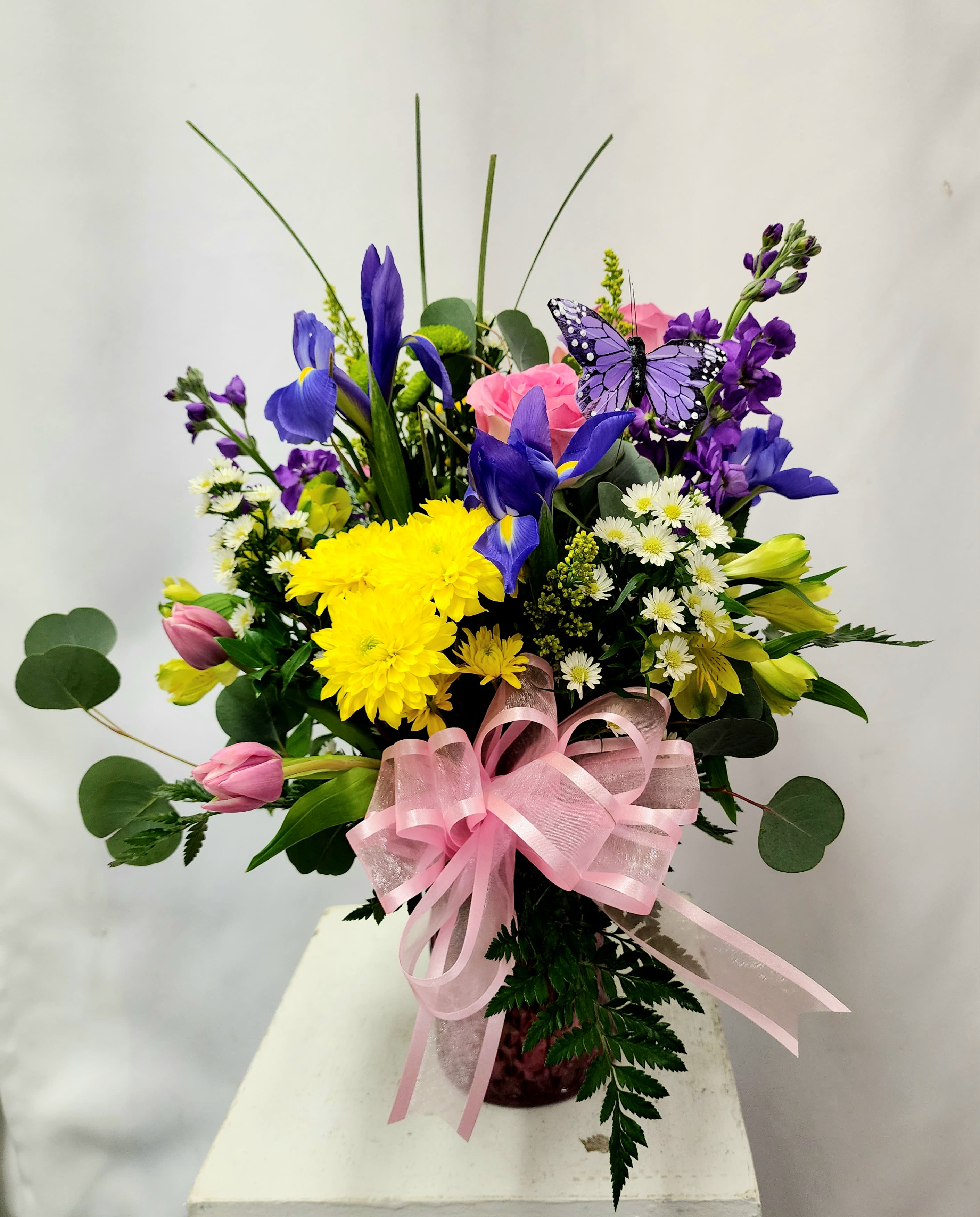 Colorful bouquet with purple irises, yellow chrysanthemums, pink tulips, and a pink ribbon