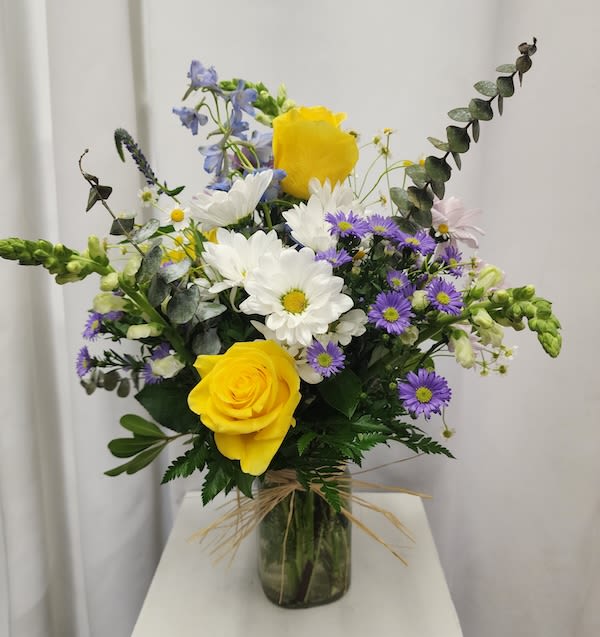 Bouquet of yellow roses, white daisies, and purple asters in a glass vase