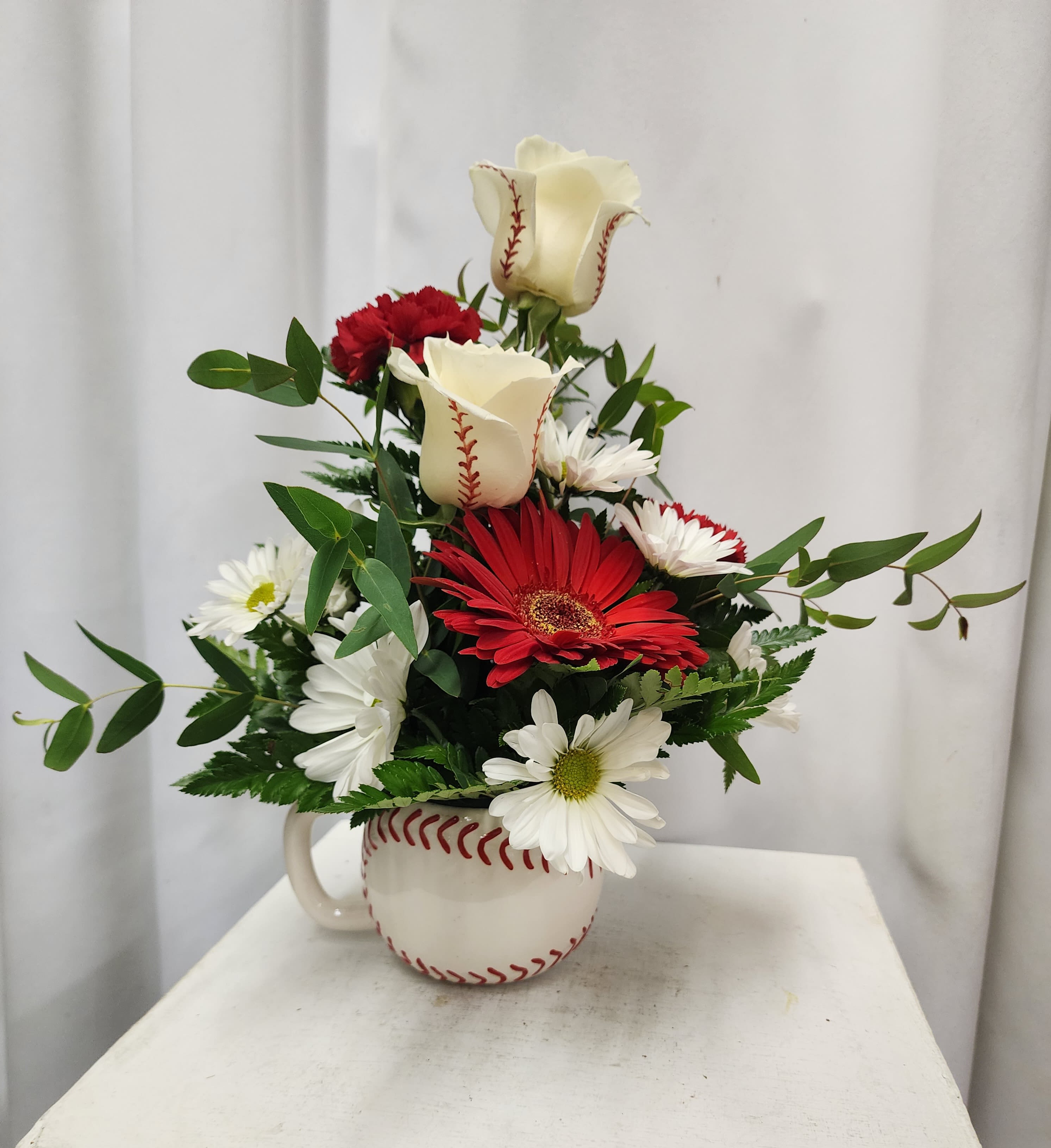 Red and white flowers arranged in a baseball-shaped mug