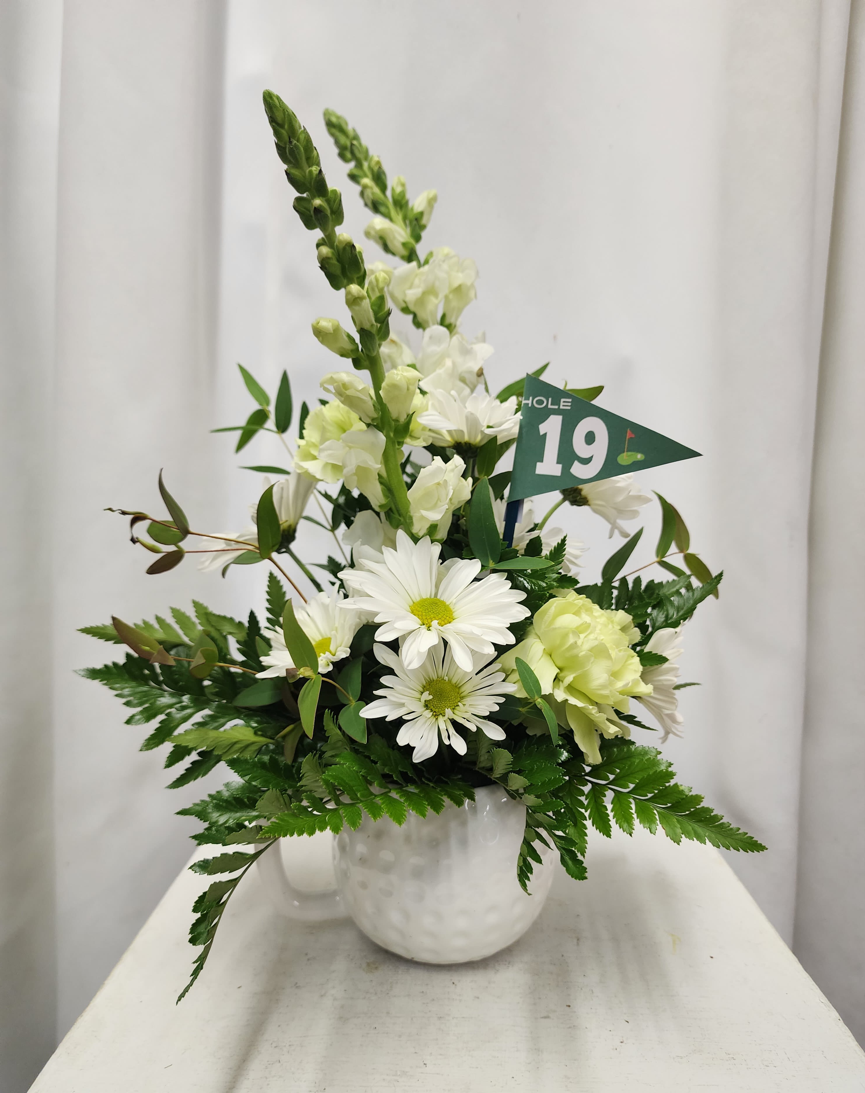 White floral arrangement in a white vase with a small green flag