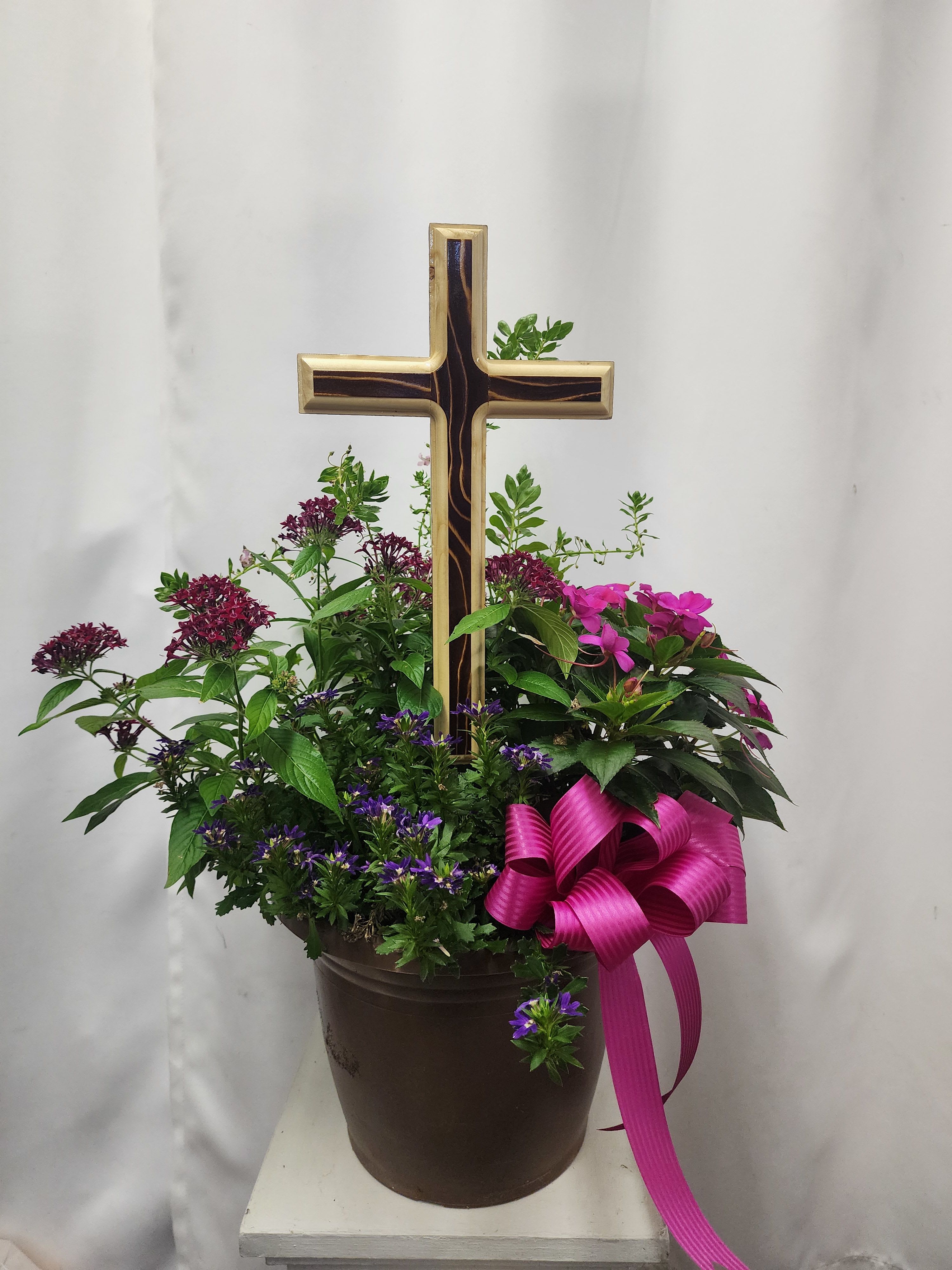 Potted floral arrangement with a wooden cross and pink ribbon