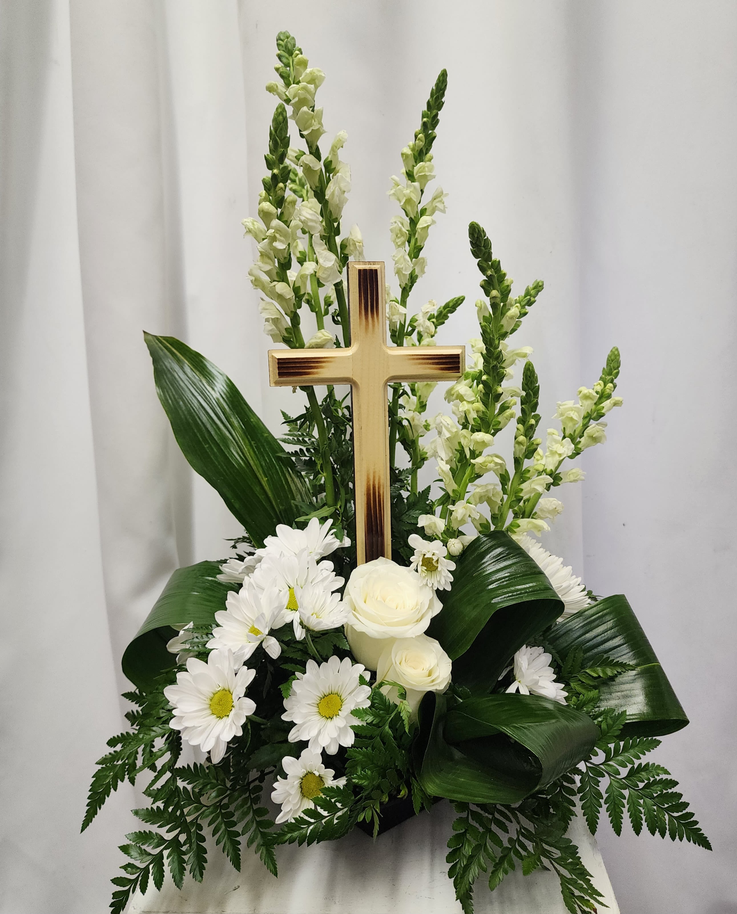 White floral arrangement with a wooden cross and daisies