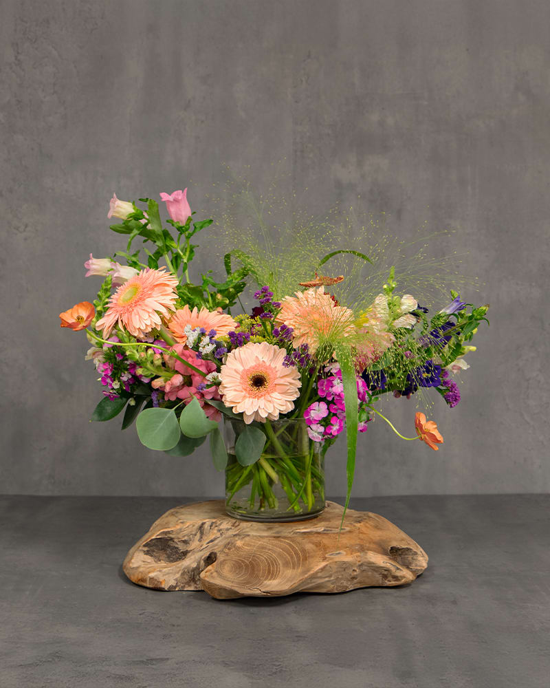 Mixed bouquet of peach, pink, purple, and orange flowers in a glass vase