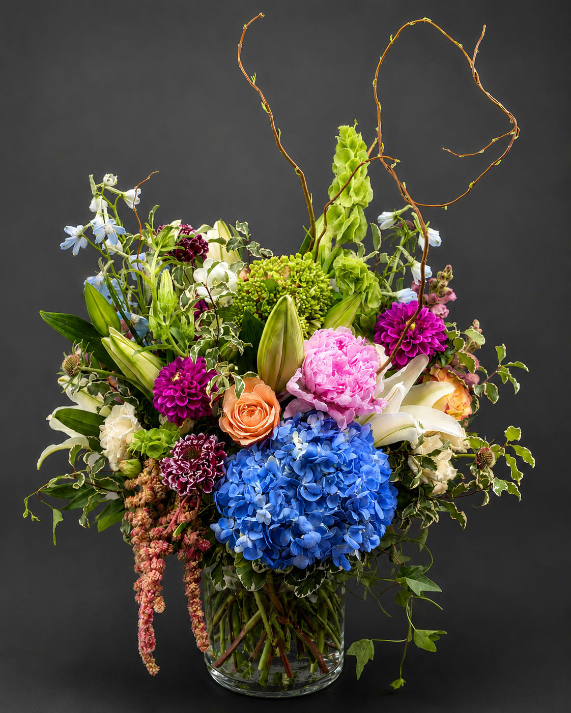 Colorful mixed flower arrangement in a clear glass vase with tall curly branches
