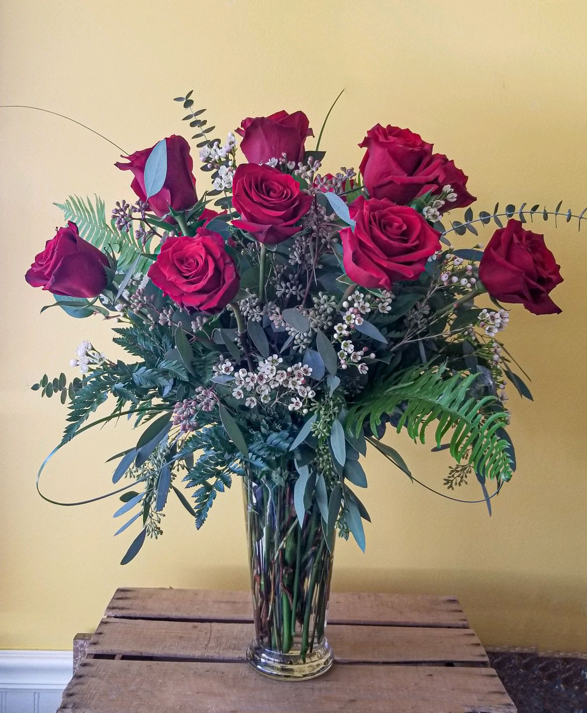 Red roses arranged in a clear glass vase with mixed greenery