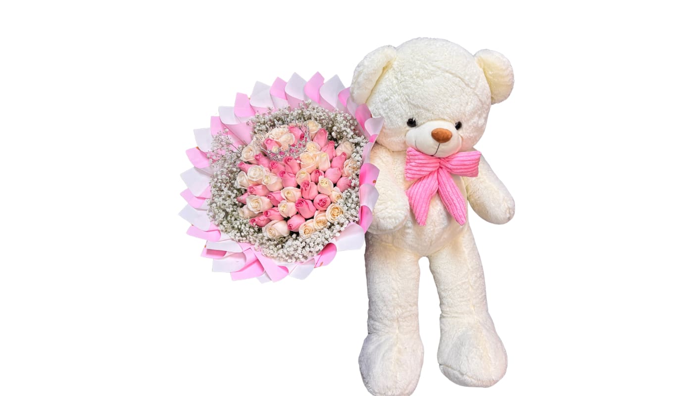 Pink and cream rose bouquet beside a white teddy bear with a pink bow