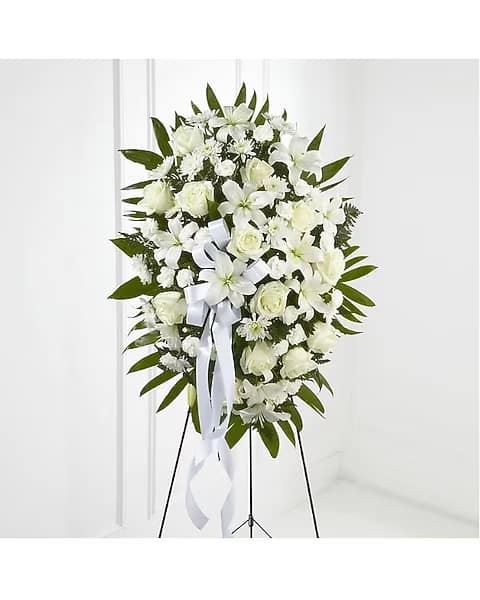 White funeral spray with lilies, roses, and a ribbon on a stand