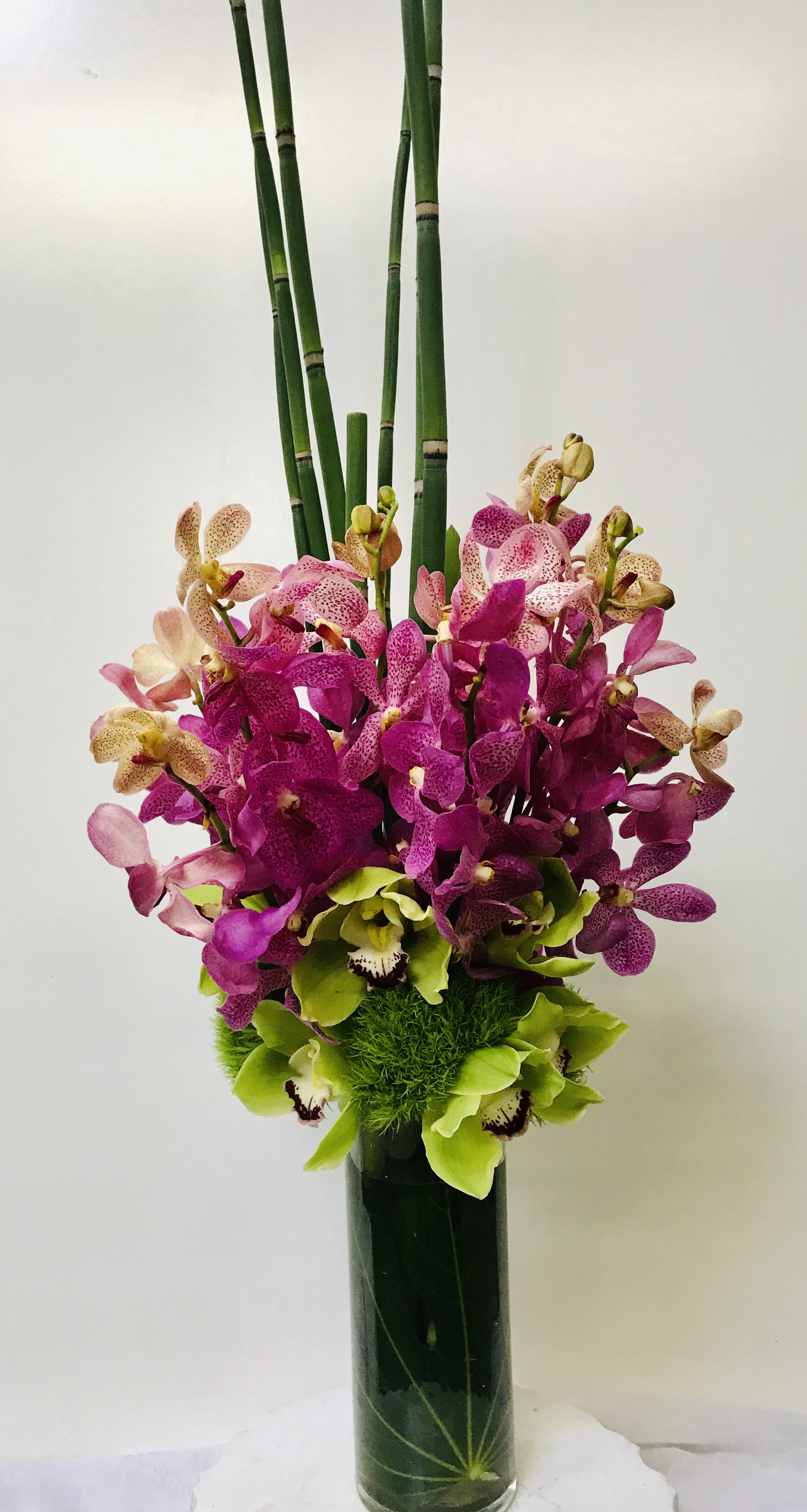 Tall orchid arrangement in a dark vase with bamboo stems