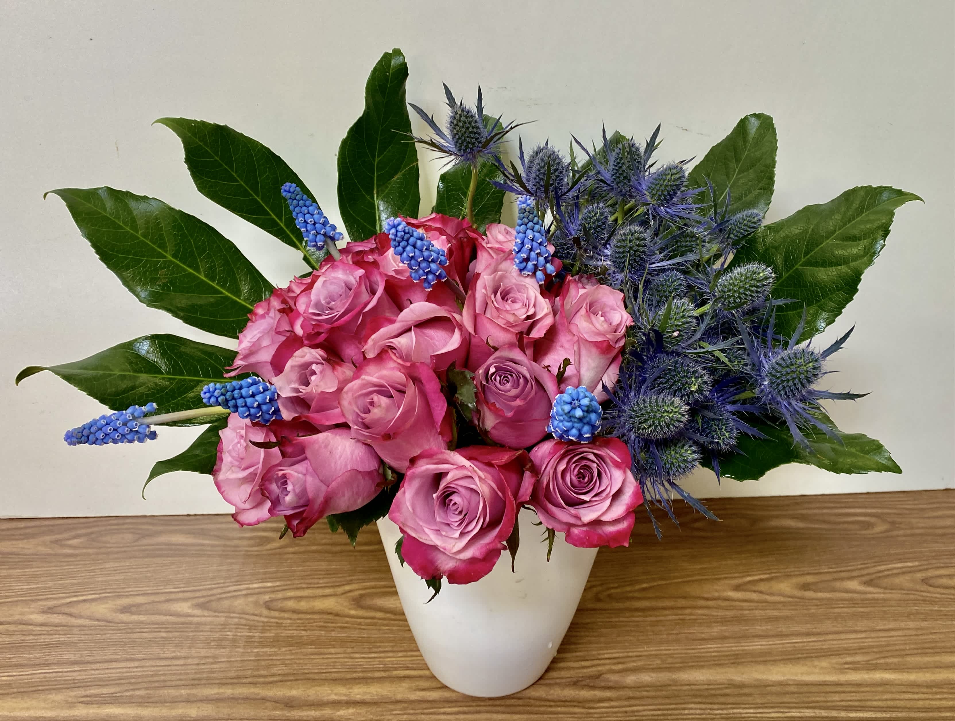 Pink roses and blue thistle in a white vase