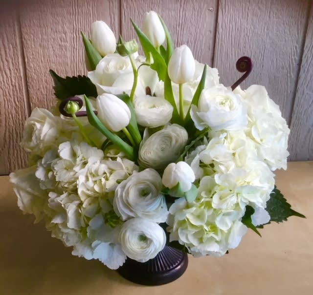 White floral arrangement with tulips, roses, ranunculus, and hydrangeas in a dark vase