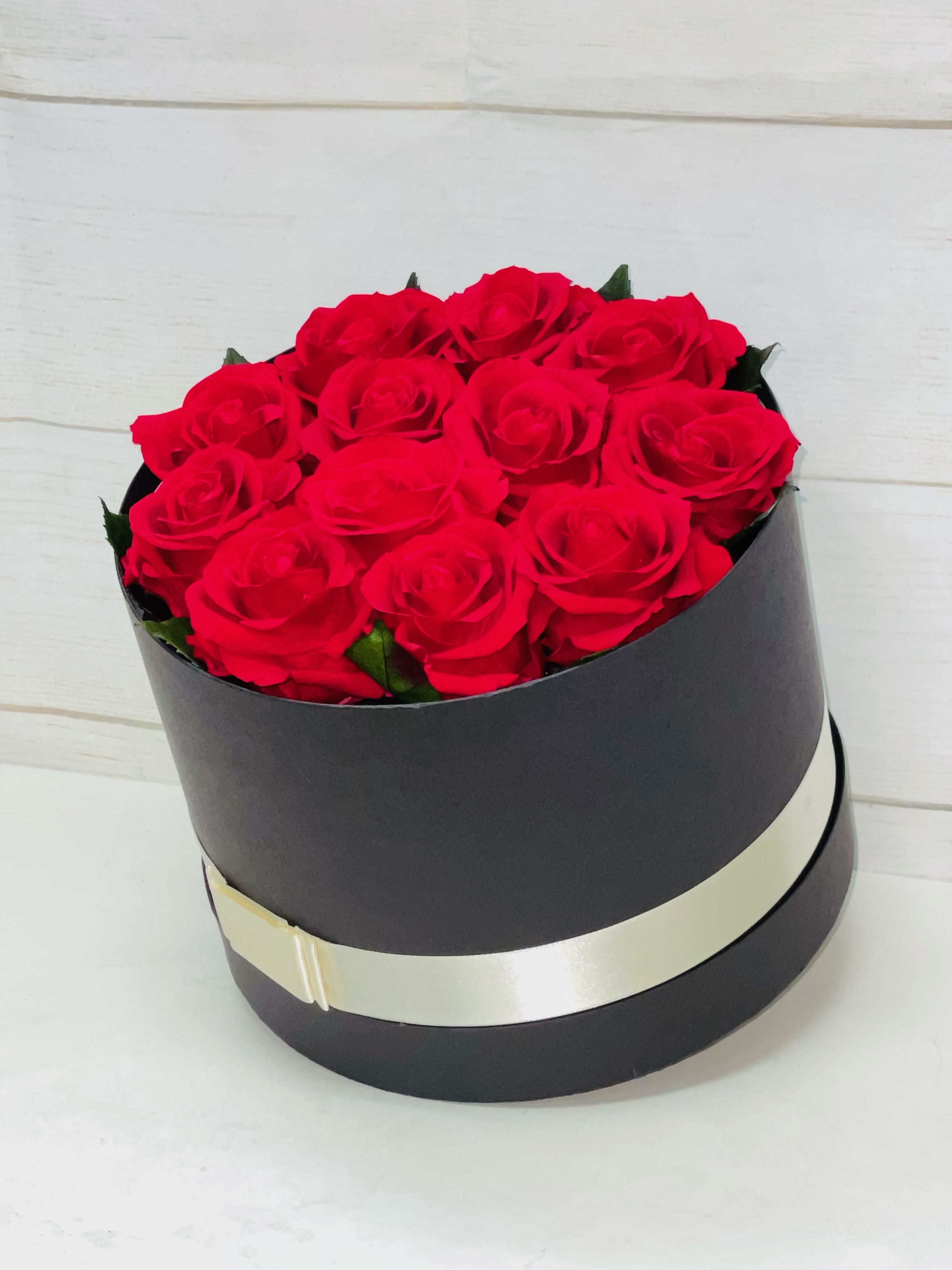 Round black box filled with red roses and wrapped with a cream ribbon