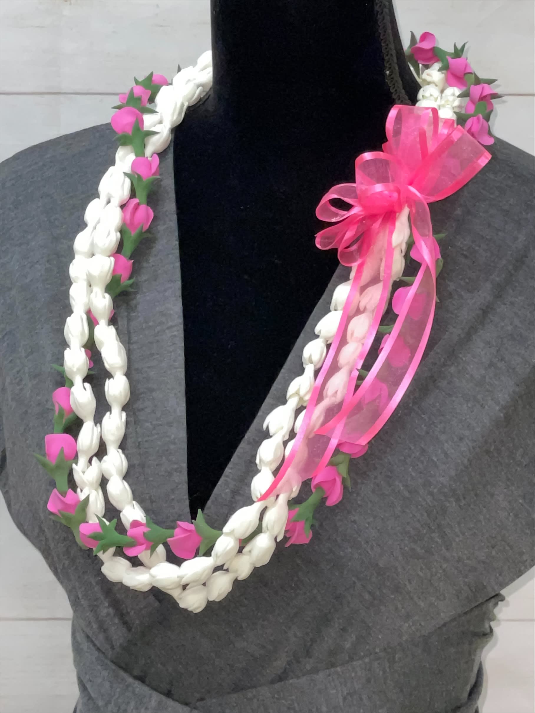 Braided white and pink floral lei with a bright pink ribbon bow displayed on a dark mannequin.