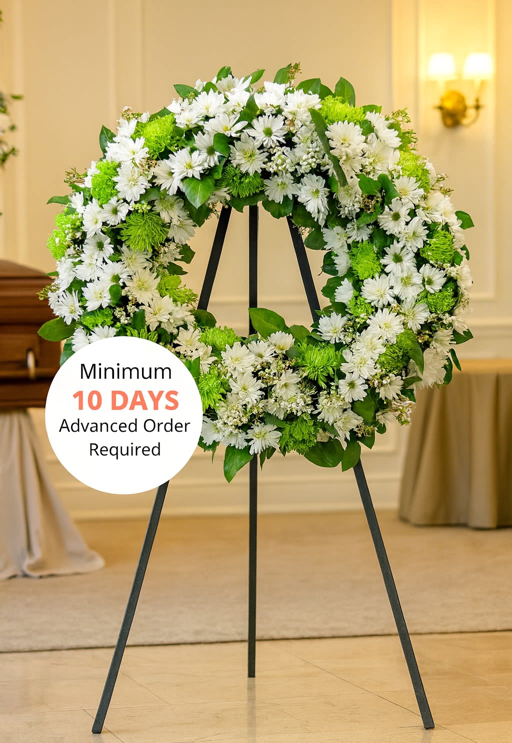 Large white and green floral wreath on a black metal easel in a chapel.