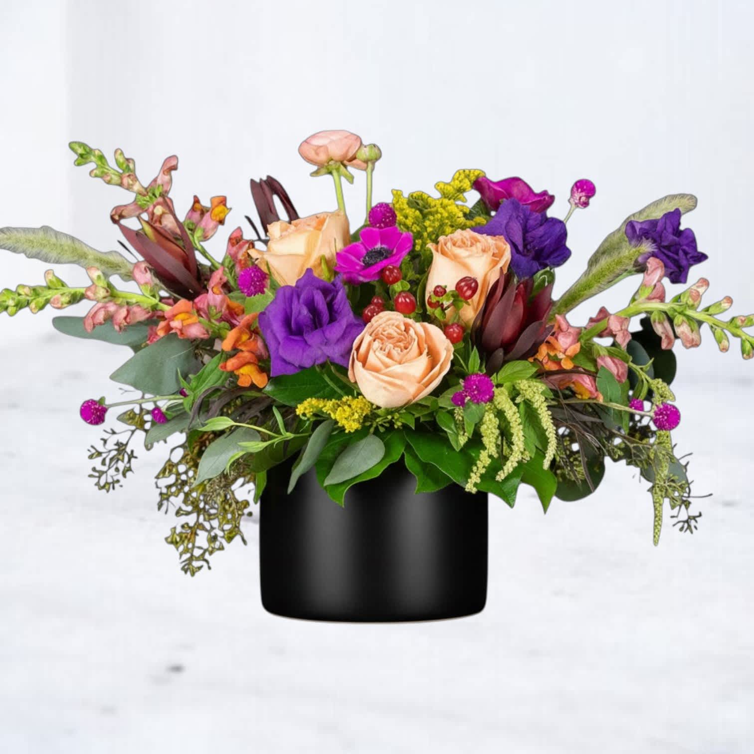 Mixed bouquet of peach roses and purple flowers in a black vase