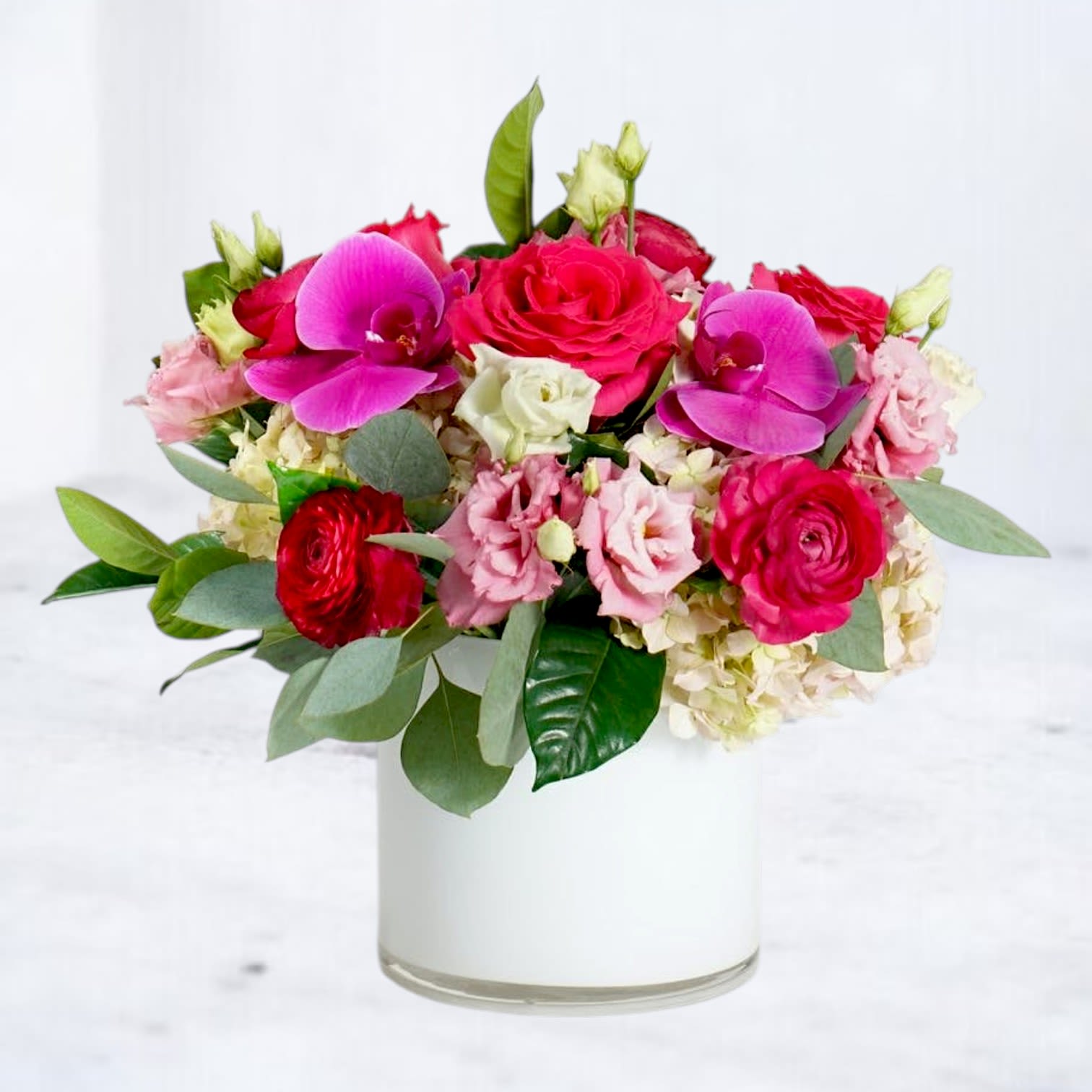 Martini - Bold, joyful, and impossible to overlook, Martini brings together vibrant pink orchids, premium roses, ranunculus, hydrangea, lisianthus, eucalyptus, and lush seasonal blooms in a modern white ceramic planter. Designed with rich texture and layered shades of fuchsia, blush, and ivory, this arrangement strikes the perfect balance between playful and polished.  Handcrafted in a keepsake ceramic planter, Martini is an exceptional choice for birthdays, anniversaries, congratulations, thank-you gifts, Mother's Day, Valentine's Day, or simply making someone's day brighter. Its contemporary garden-inspired style makes it equally at home in a modern living room, office, or dining table.  Each arrangement is designed using the freshest flowers available. Seasonal substitutions may occasionally be necessary, but our designers will always preserve the luxurious color palette, premium quality, and signature style of Martini.  Available for hand delivery throughout Houston, Magnolia, Montgomery, The Woodlands, Conroe, Spring, Tomball, Cypress, Willis, Plantersville, and surrounding communities.