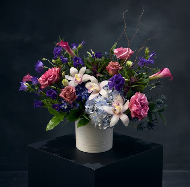 Mixed bouquet of pink, purple, and white flowers in a white vase