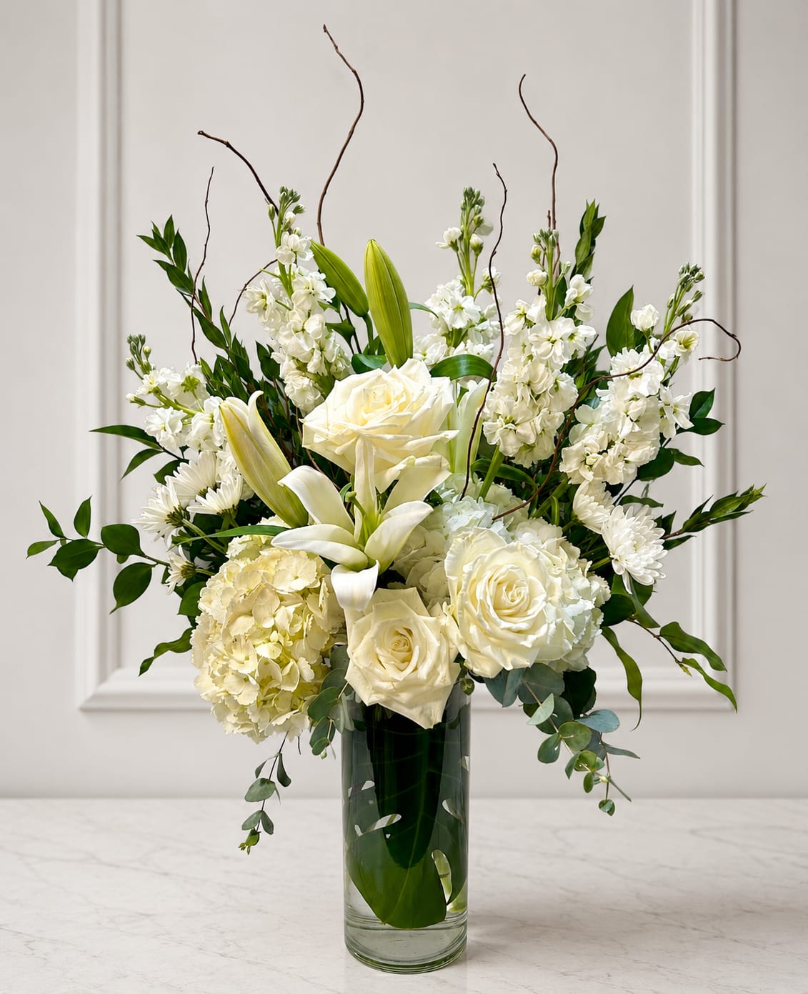 White roses and lilies arranged in a tall glass vase