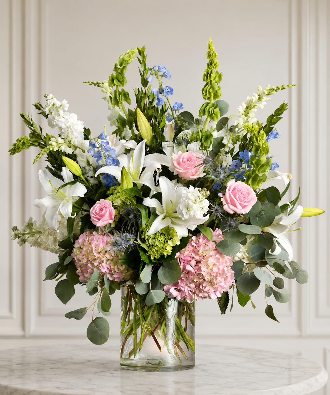 Mixed bouquet of white lilies, pink roses, and blue flowers in a glass vase