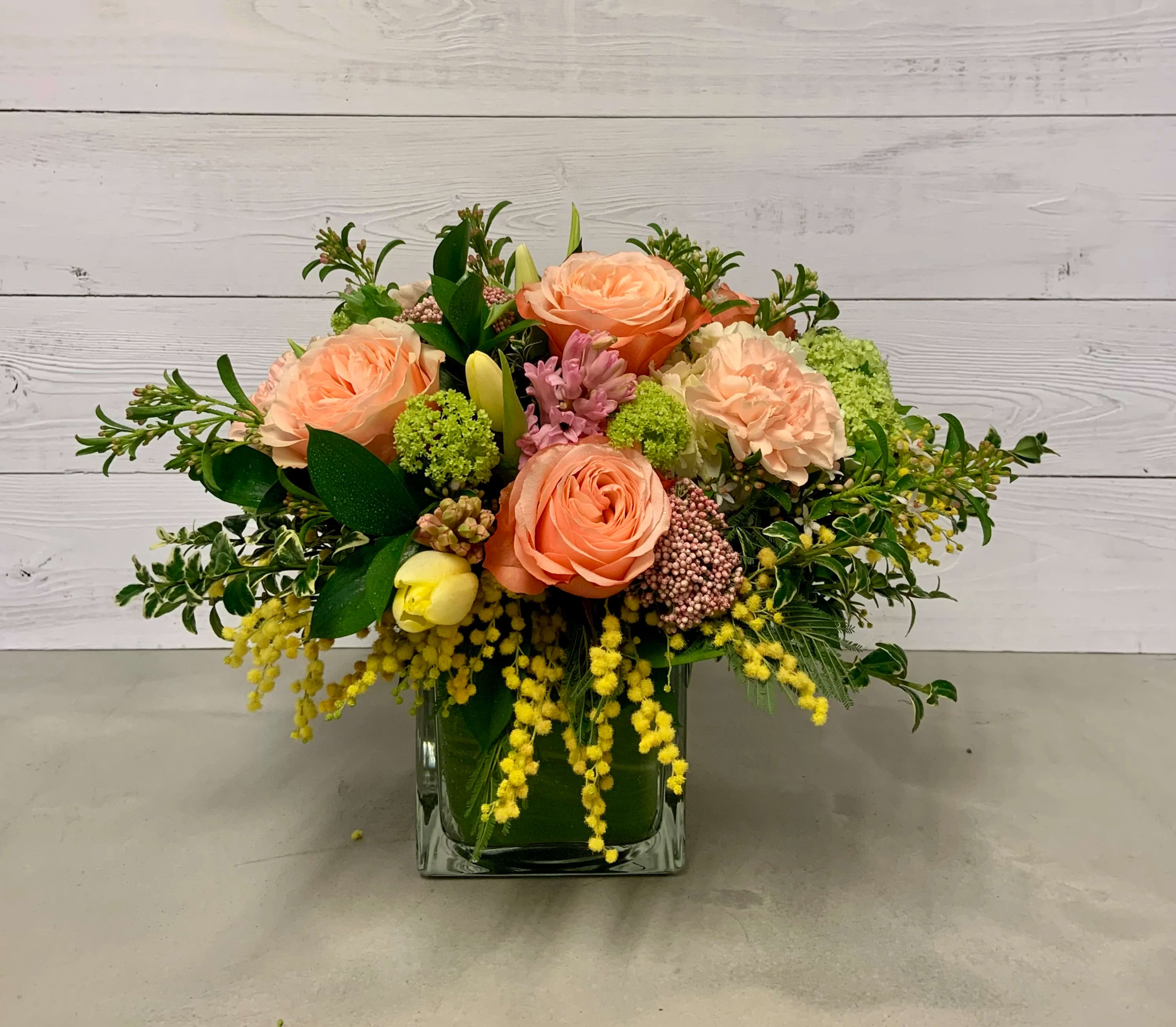 Peach roses and mixed blooms arranged in a square glass vase