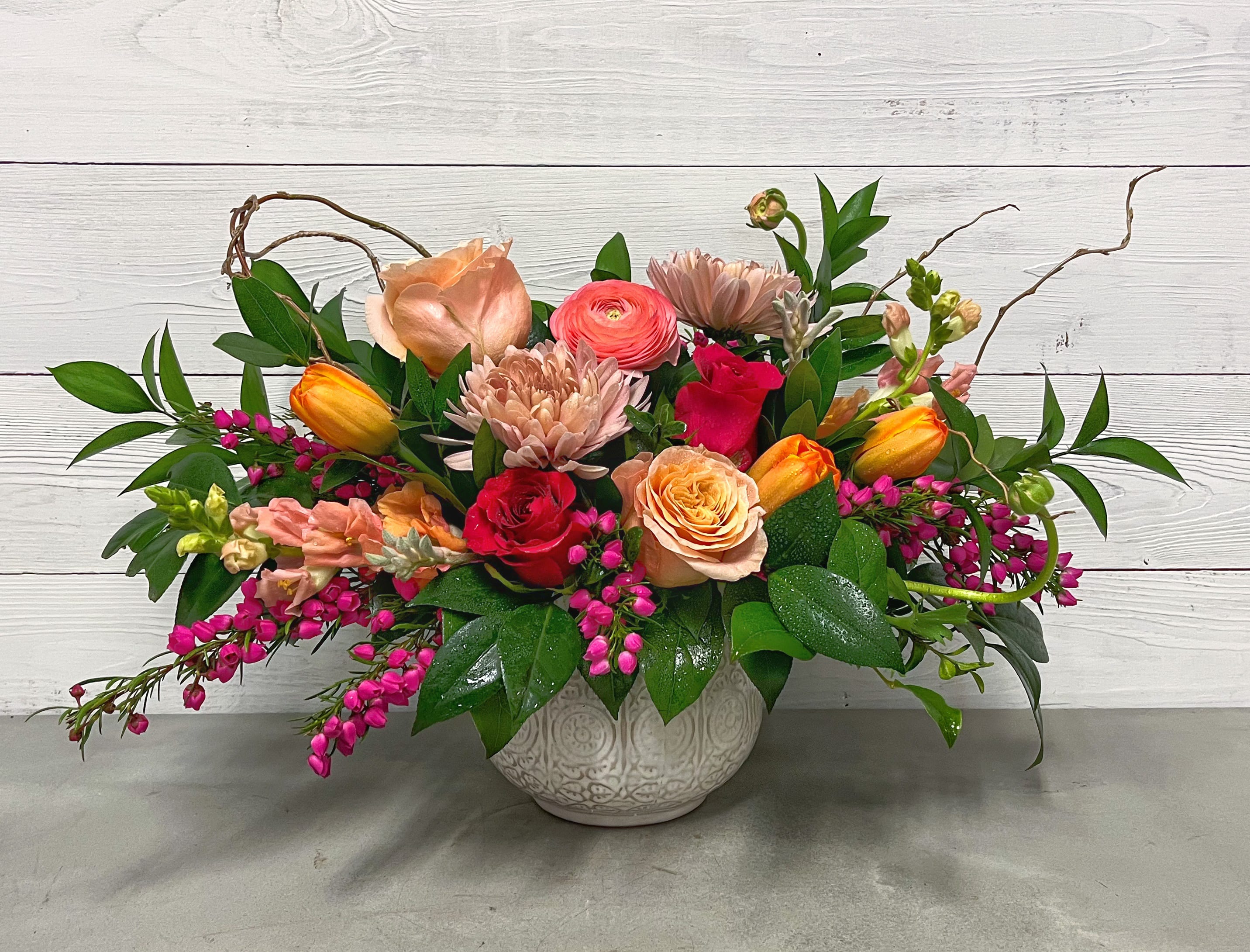 Mixed bouquet in a white ceramic vase with pink, peach, and orange flowers