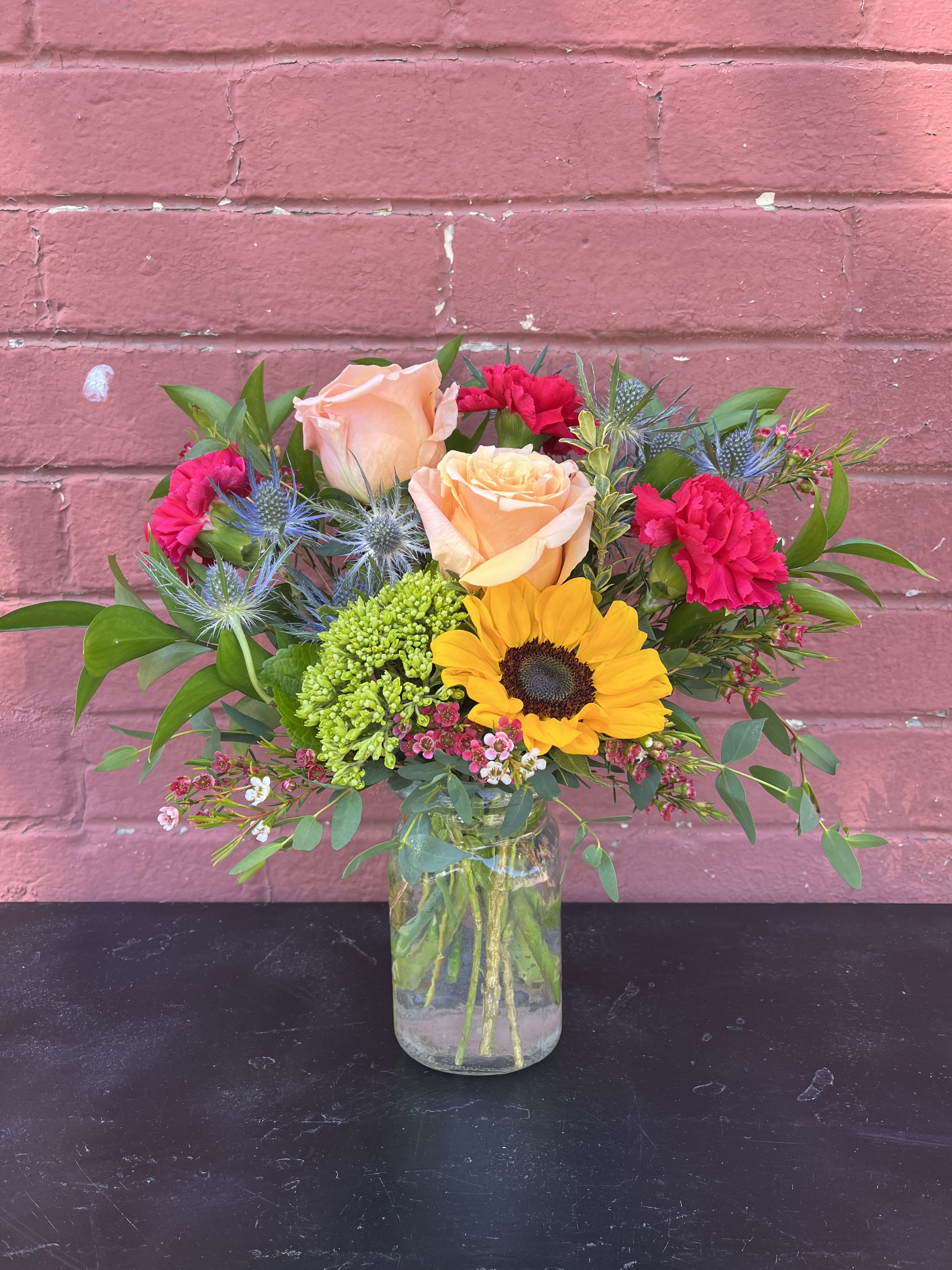 Mixed bouquet with roses, sunflower, and pink carnations in a glass vase