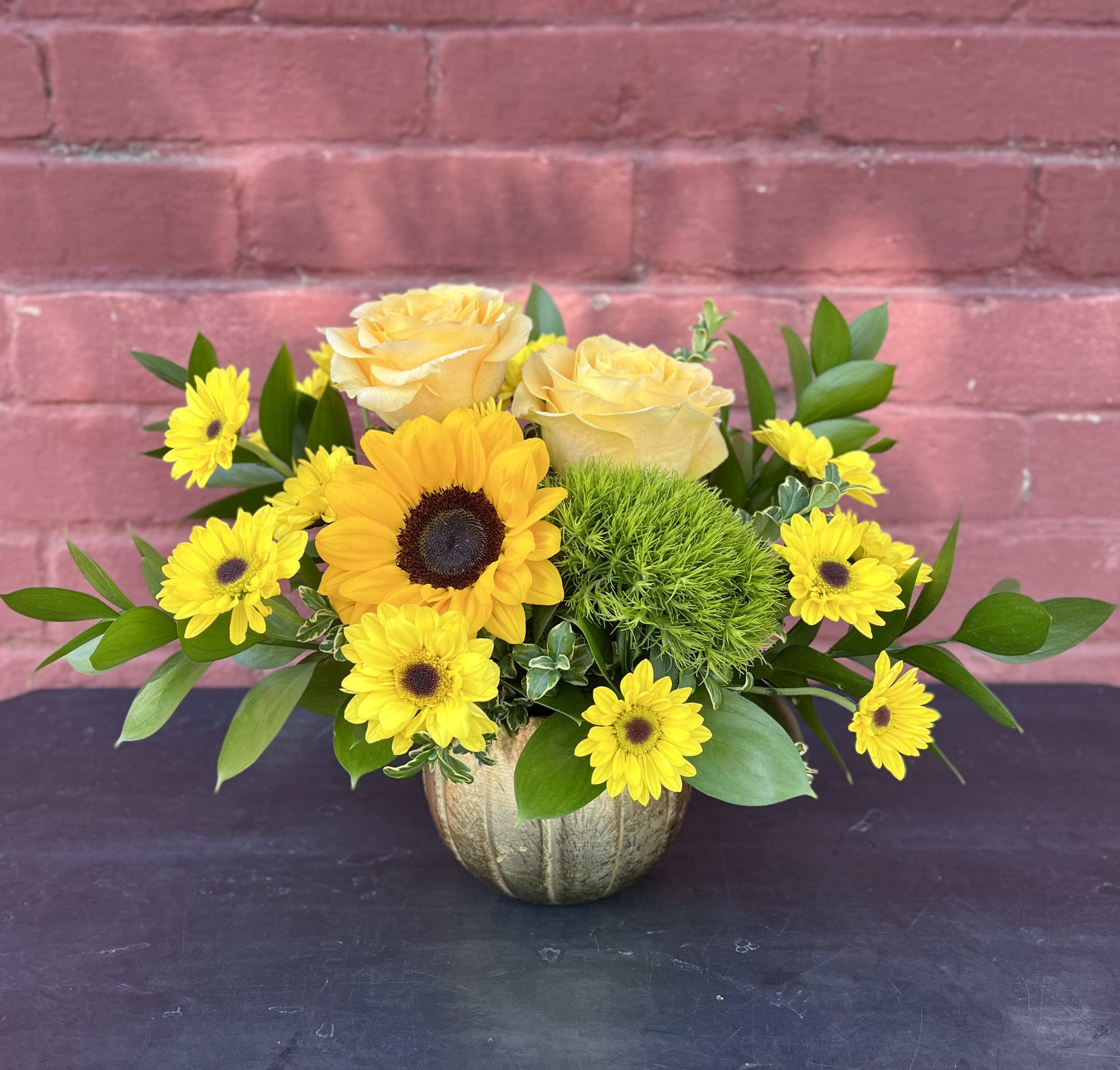 Daphne - This arrangement features a mix of roses, sunflowers, chrysanthemums, dianthus, greens, and filler in a white ceramic vase. 