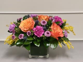 Orange roses and purple flowers in a square glass vase