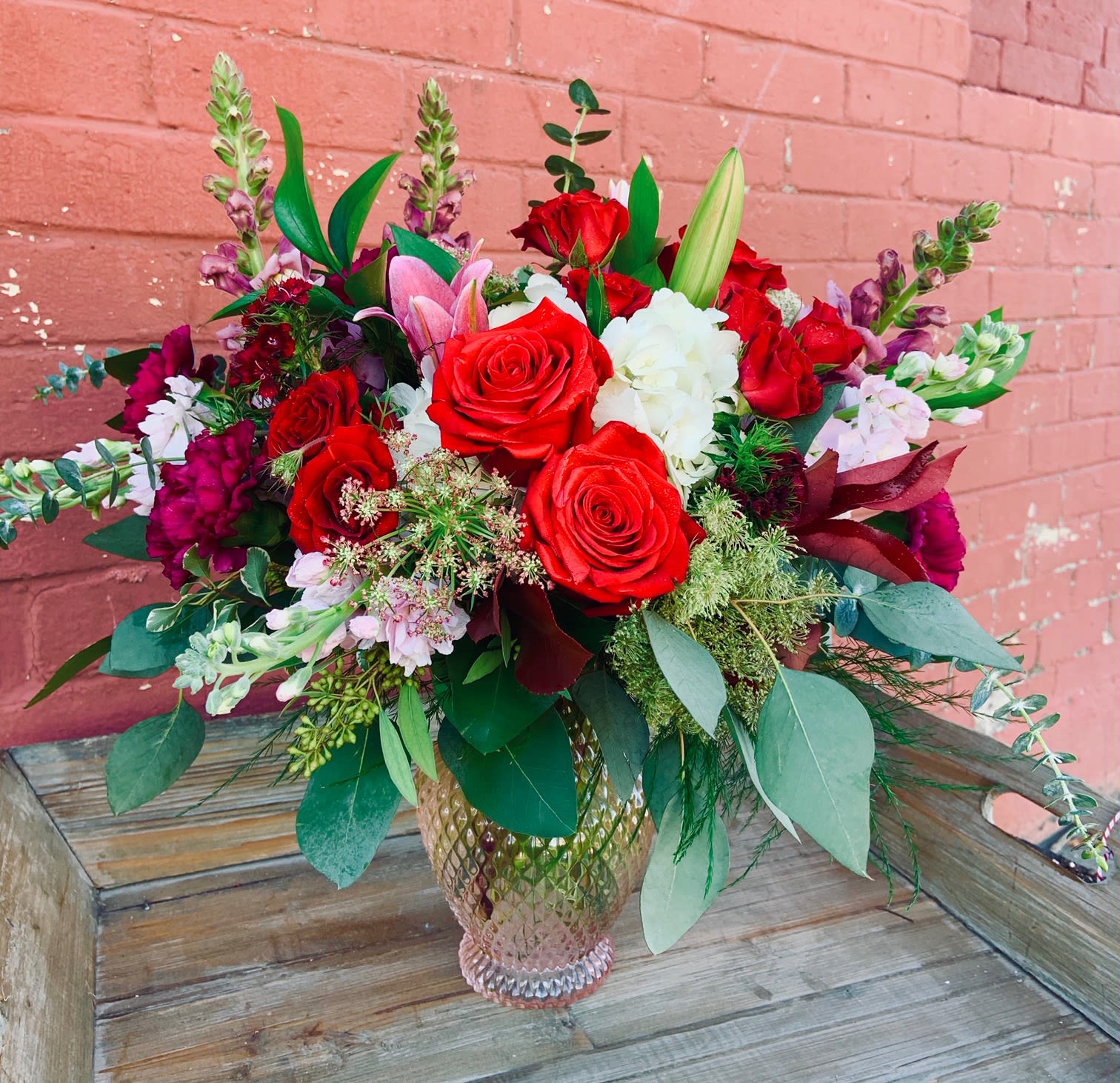 Bouquet of red roses, white blooms, and pink lilies in a glass vase