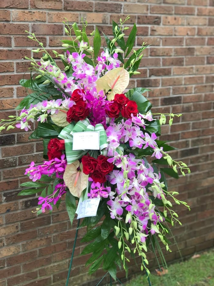 Standing spray of purple orchids, red roses, and pale anthuriums on a display easel