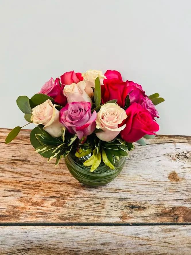 Round arrangement of pink, cream, and lavender roses in a clear glass bowl vase