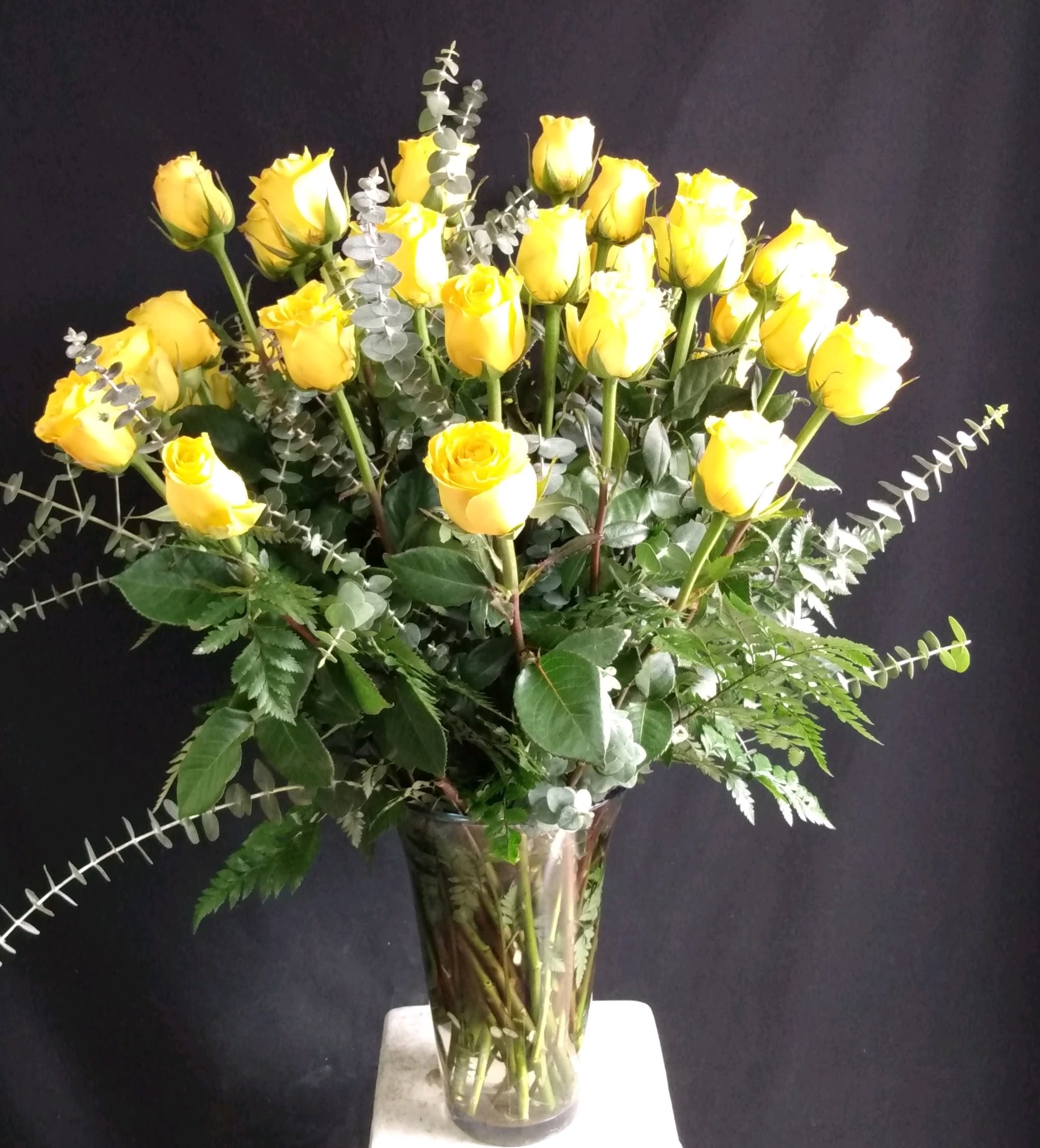 Yellow roses arranged in a clear glass vase with eucalyptus foliage