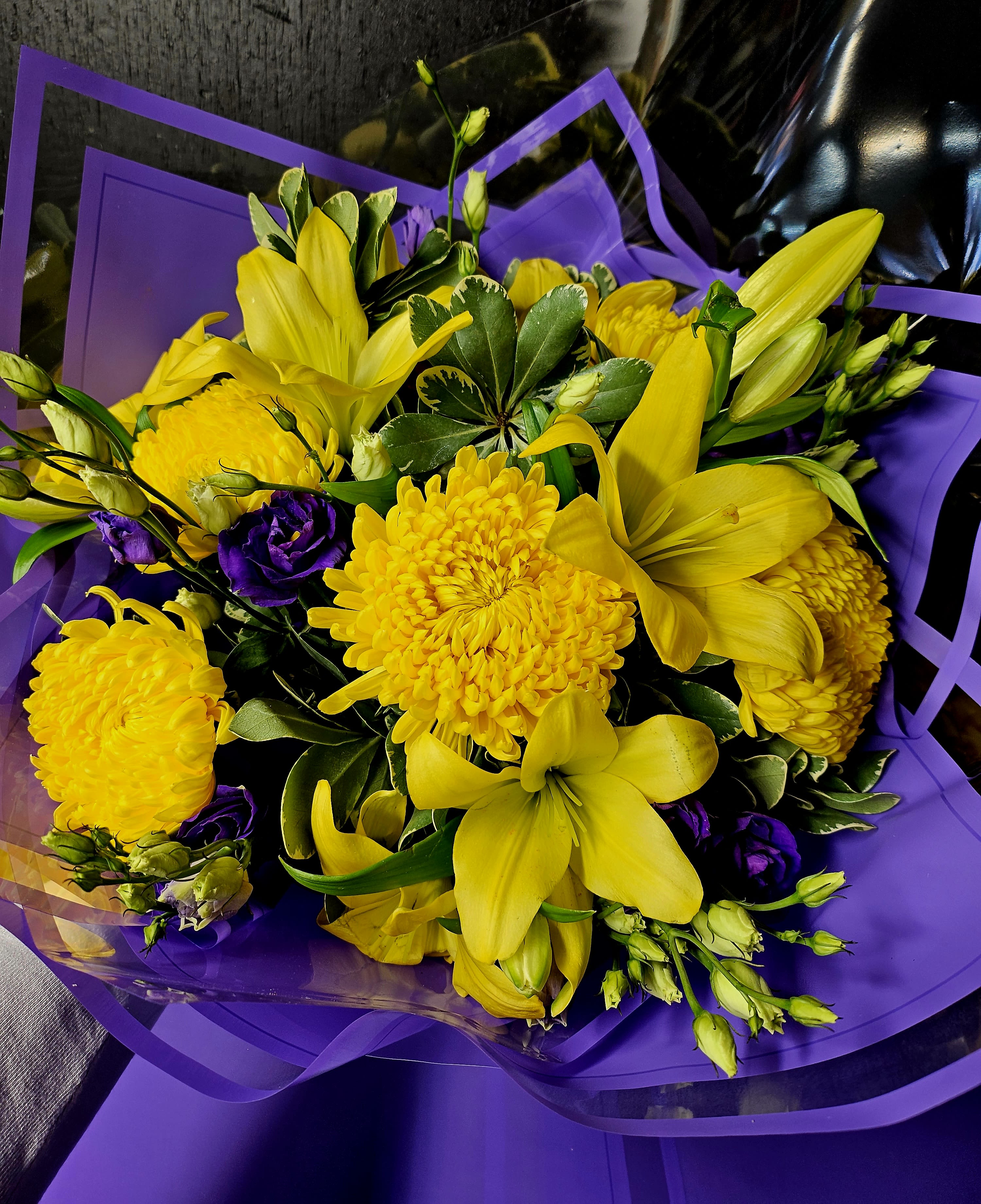 Yellow lilies and chrysanthemums with purple flowers wrapped in purple paper