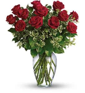 Red roses arranged in a clear glass vase with mixed greenery