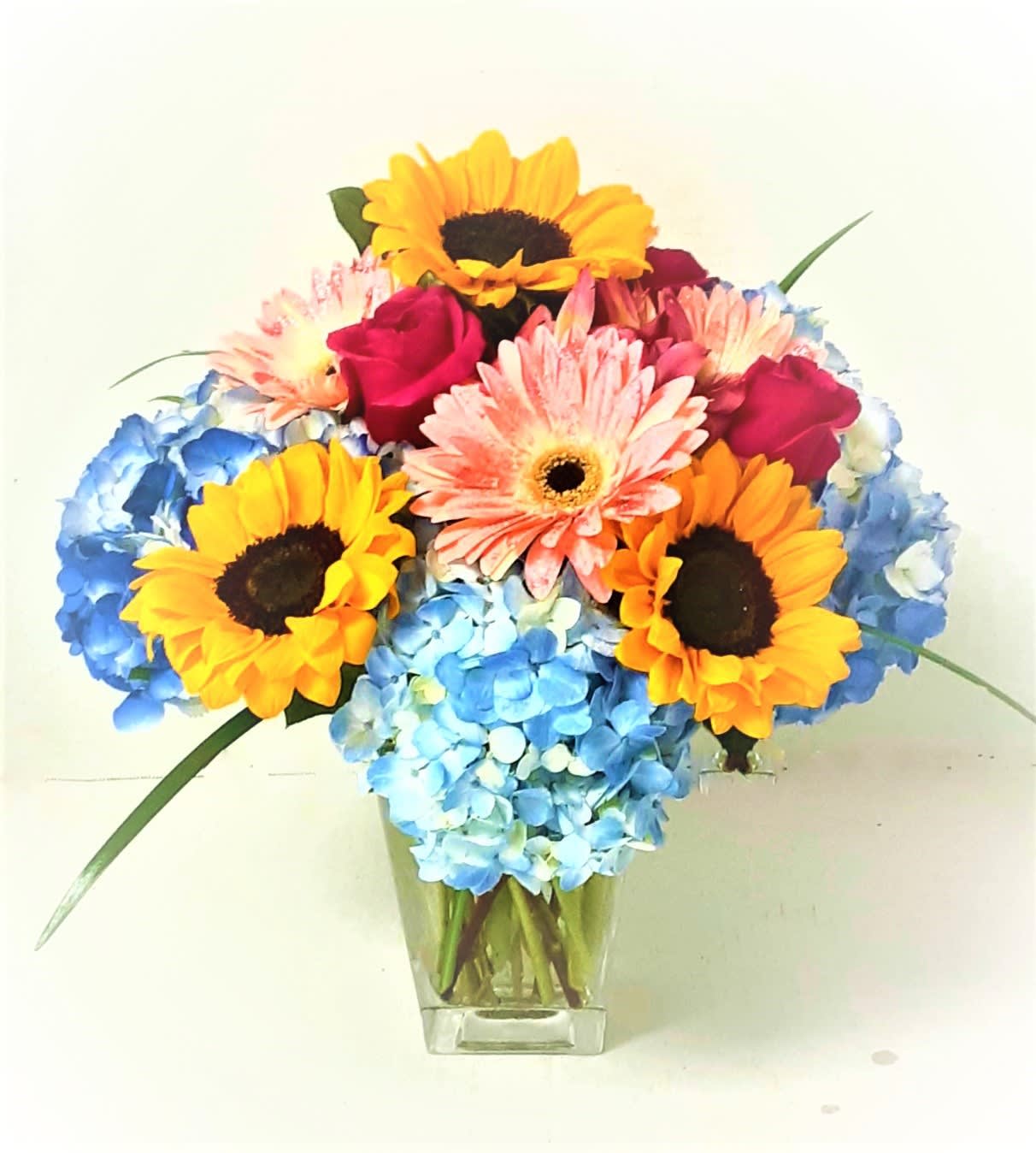 Bouquet of sunflowers, pink gerberas, roses, and blue hydrangeas in a clear vase