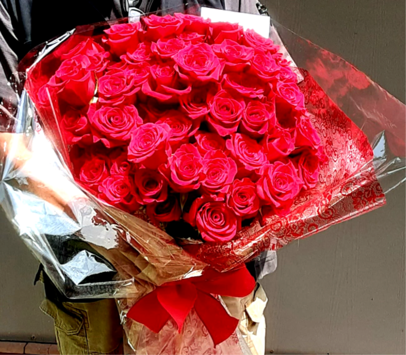 Large bouquet of bright red roses wrapped in shiny paper with a red ribbon