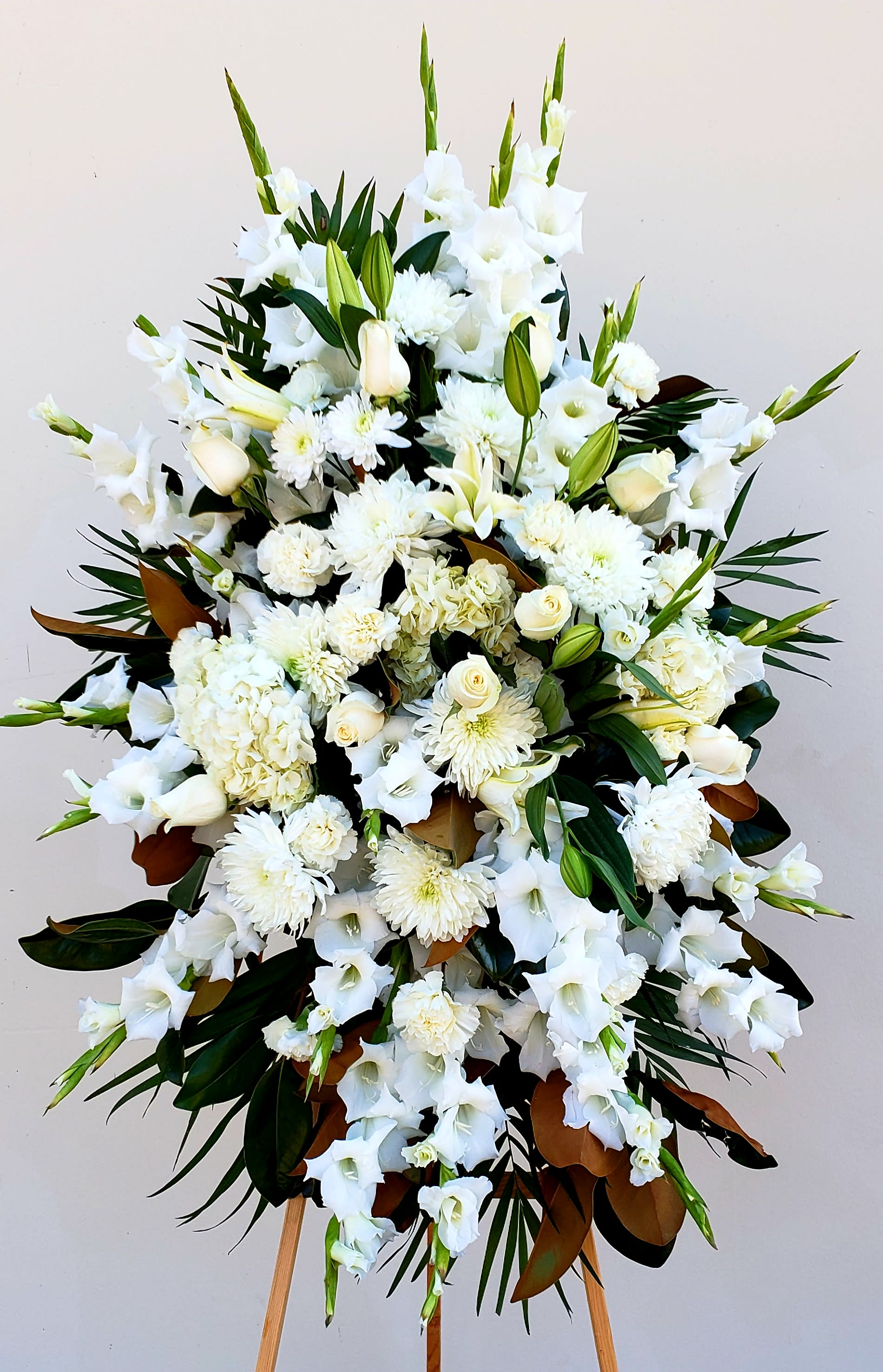 Large white funeral spray with lilies, roses, and chrysanthemums on an easel