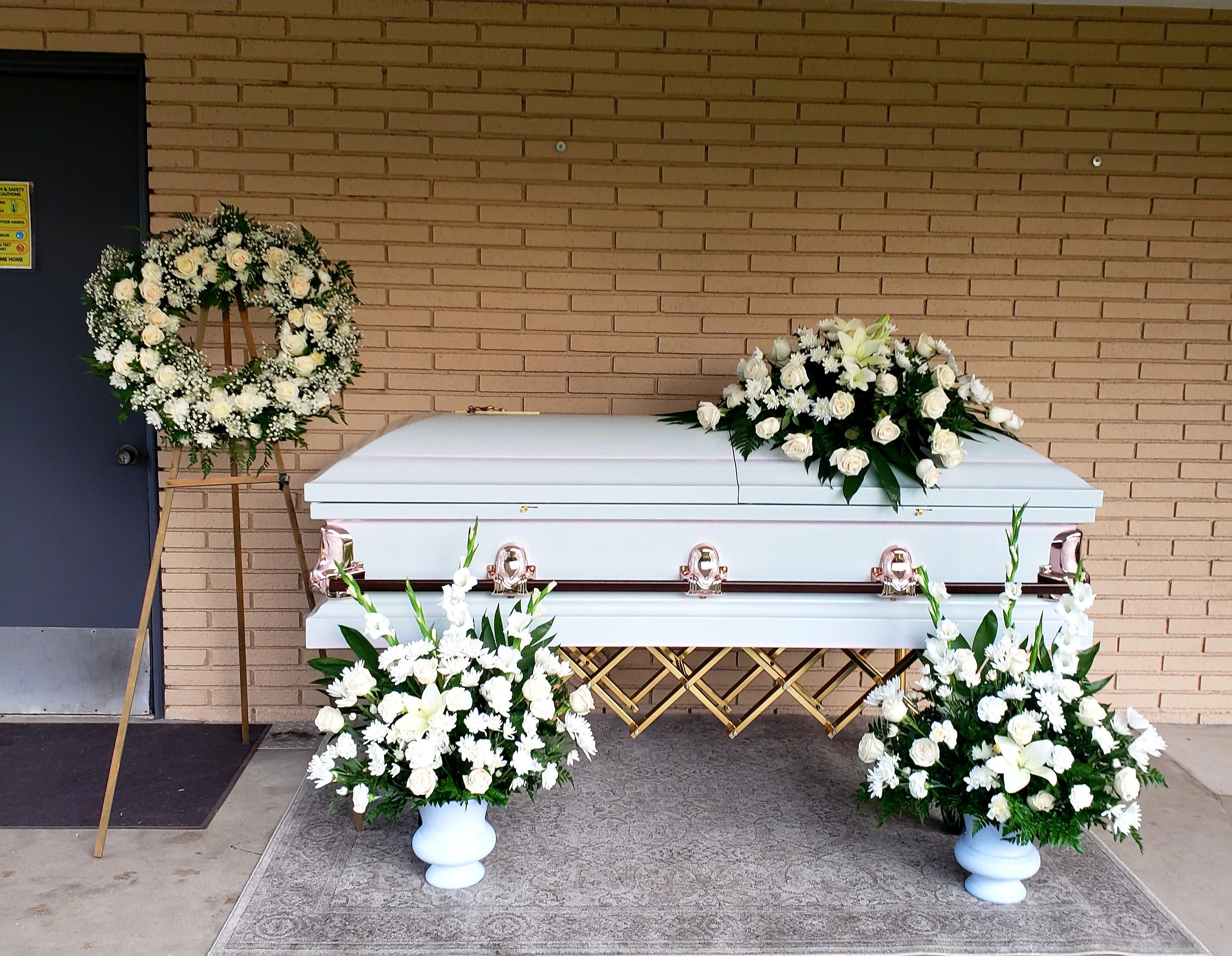 White casket with white floral sprays and a wreath on easels