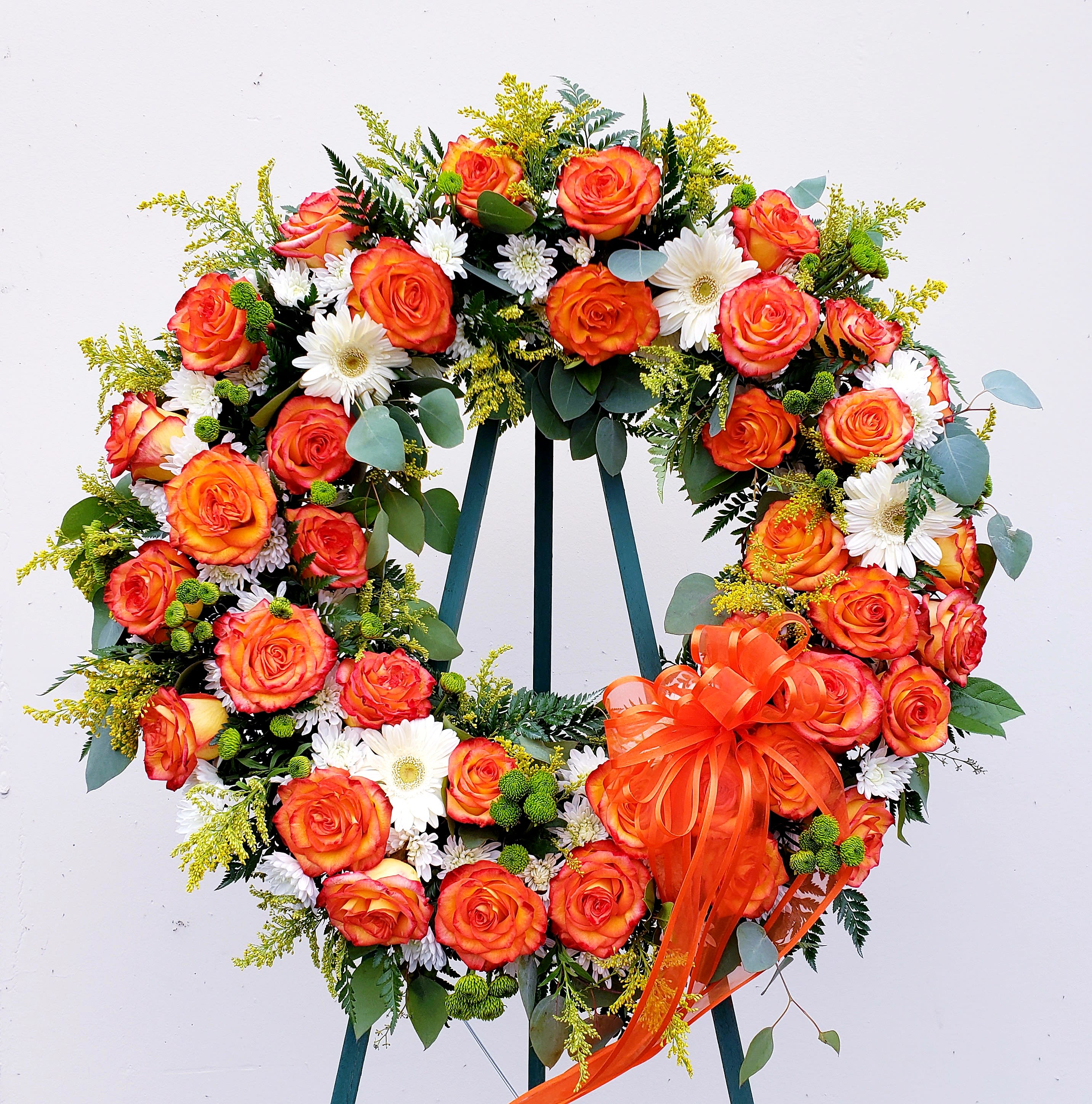 Heart-shaped wreath of orange roses and white daisies with an orange ribbon